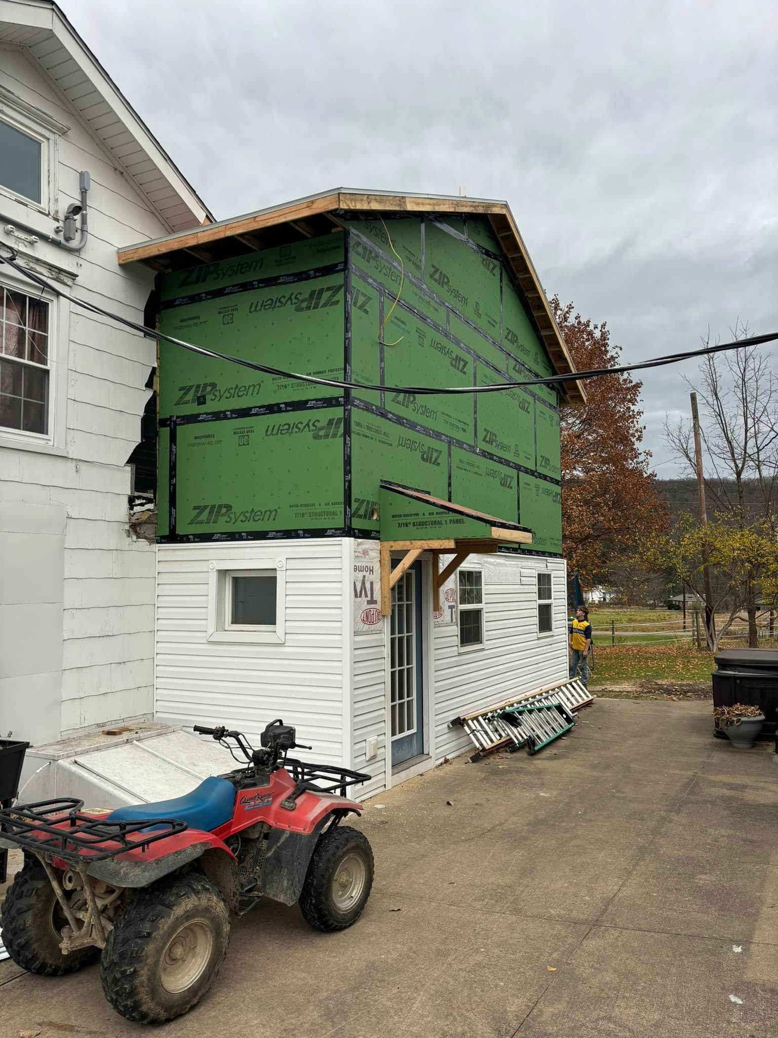A two-story building addition under construction, featuring green sheathing on the top floor and white siding below.