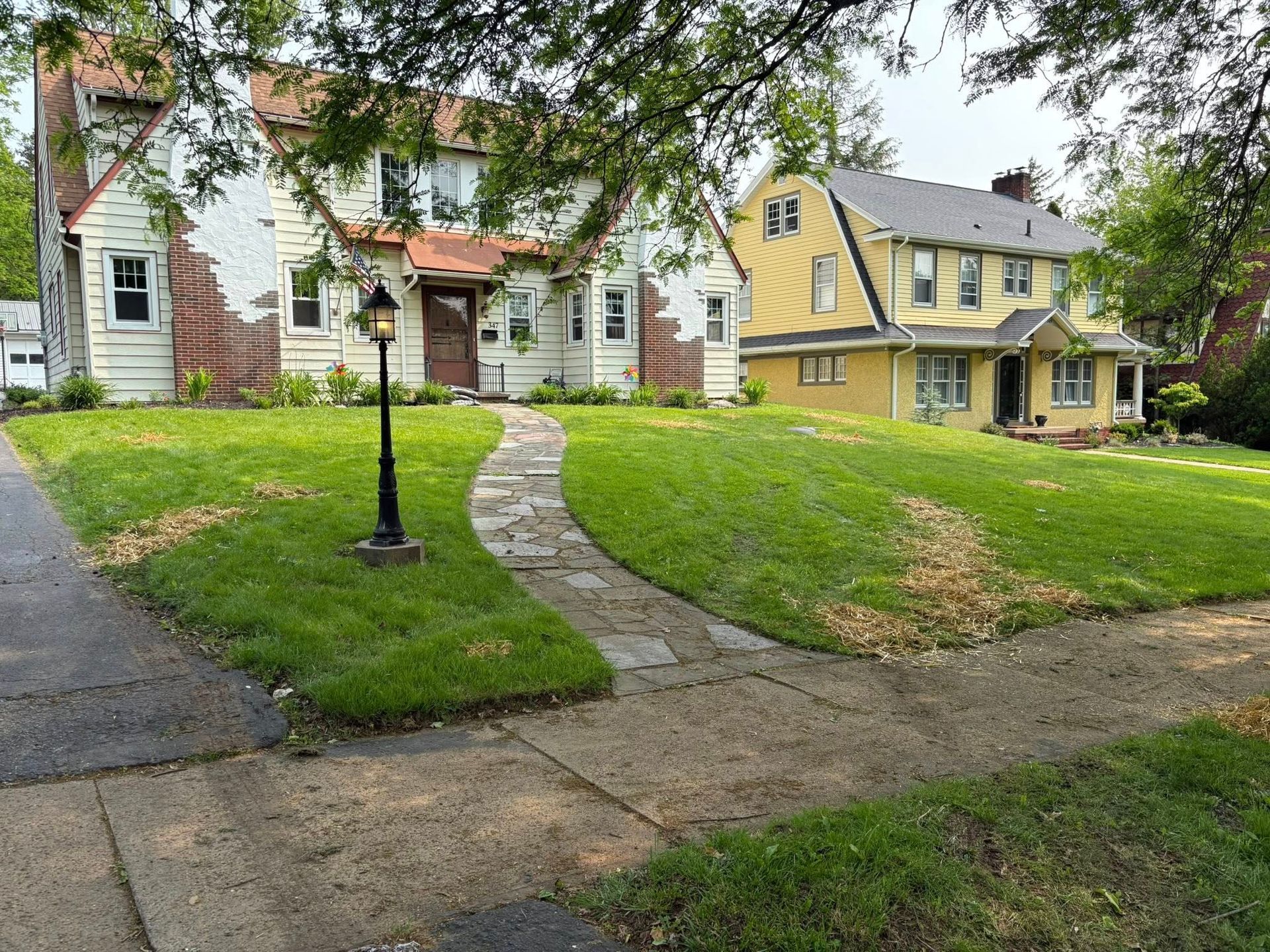 A grassy front yard with a stone path leading to a white house, with a yellow house visible in the background.