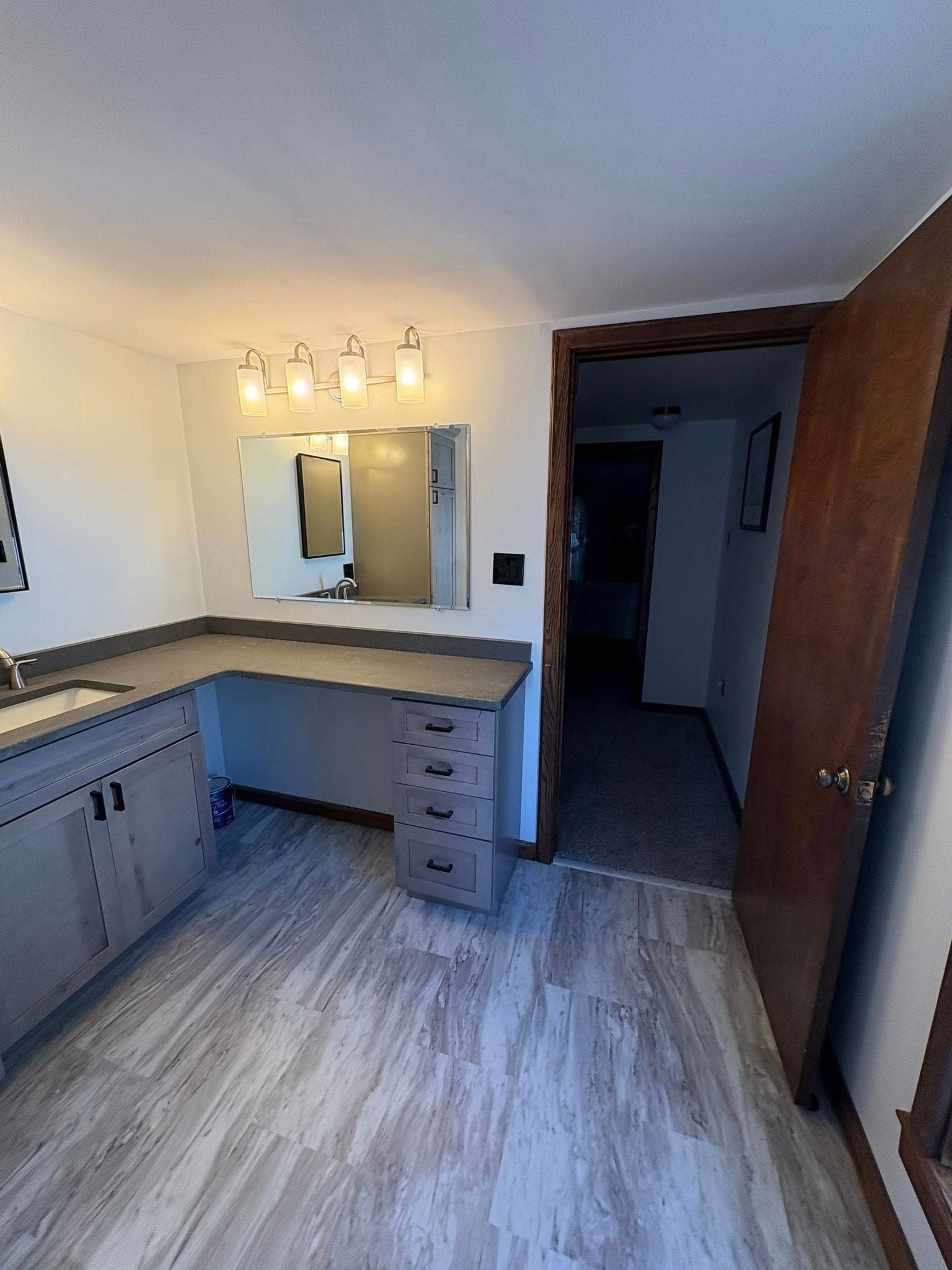 A brown shed with double wooden doors and a white-trimmed window sits on a gravel lot near a forested hillside.