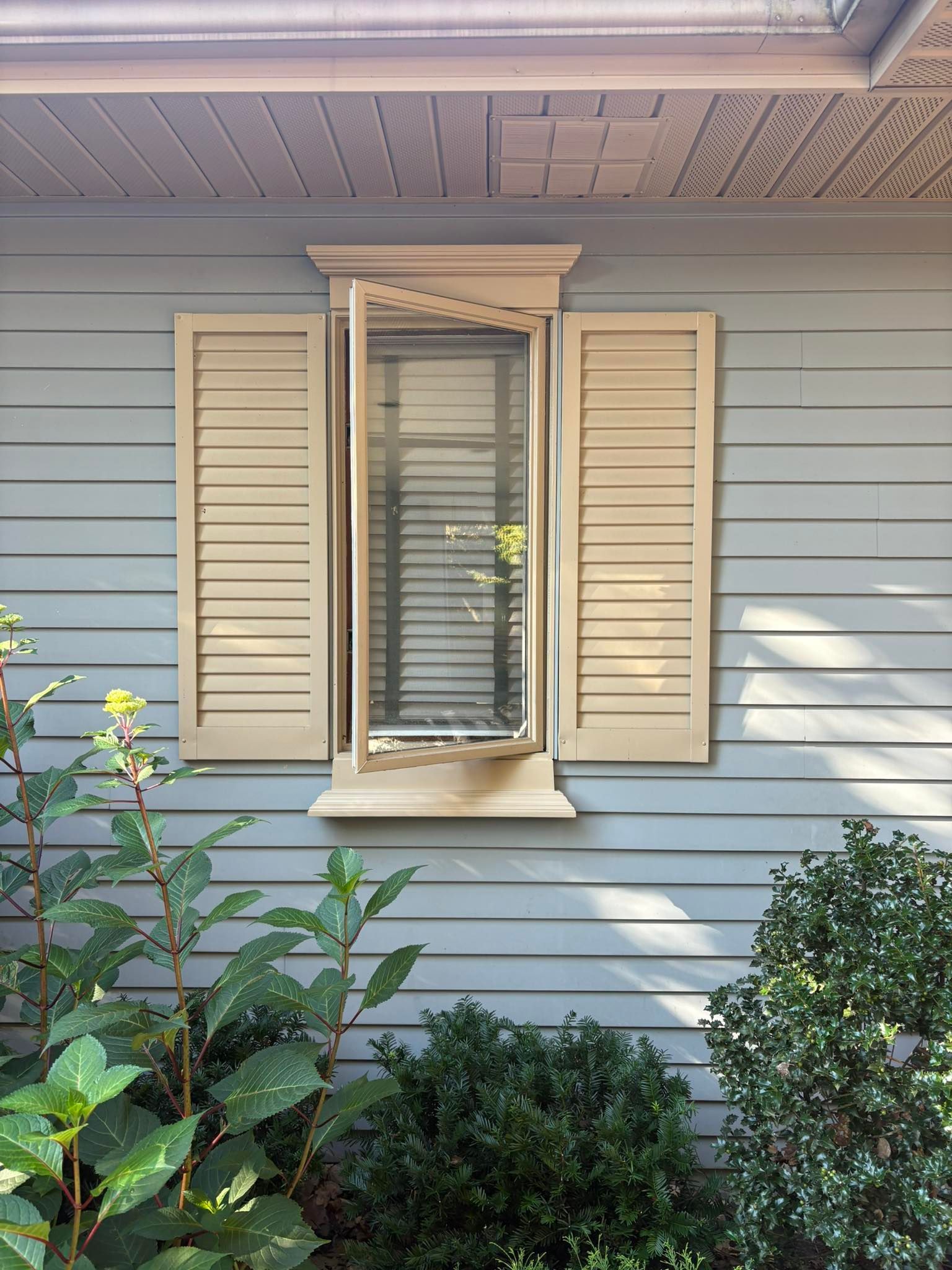 A light blue house exterior featuring a rectangular window with open cream shutters and horizontal siding.