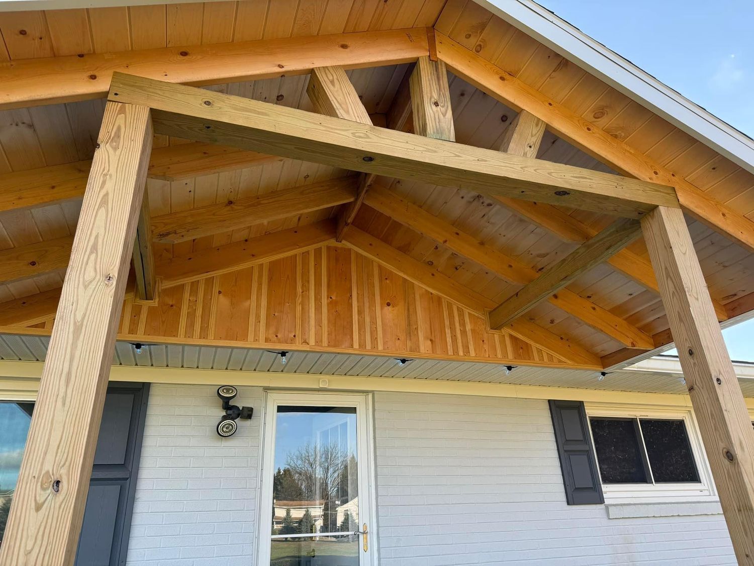 A wooden porch addition featuring a gabled roof frame attached to the front of a light-colored house.