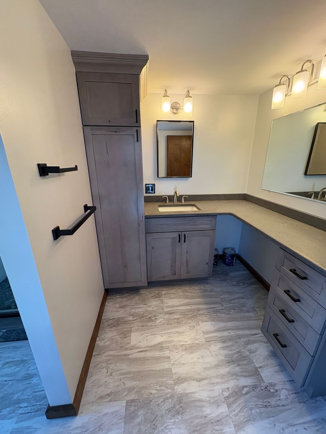 A bathroom vanity with wood cabinetry, a sink, light fixtures, a mirror, and a wall-mounted towel bar.