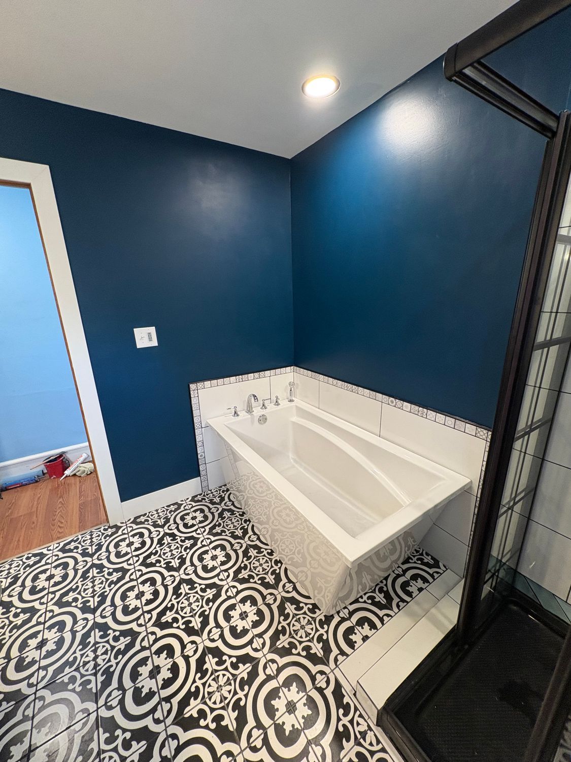 A modern bathroom featuring a white bathtub, dark blue walls, and patterned black-and-white tile flooring.
