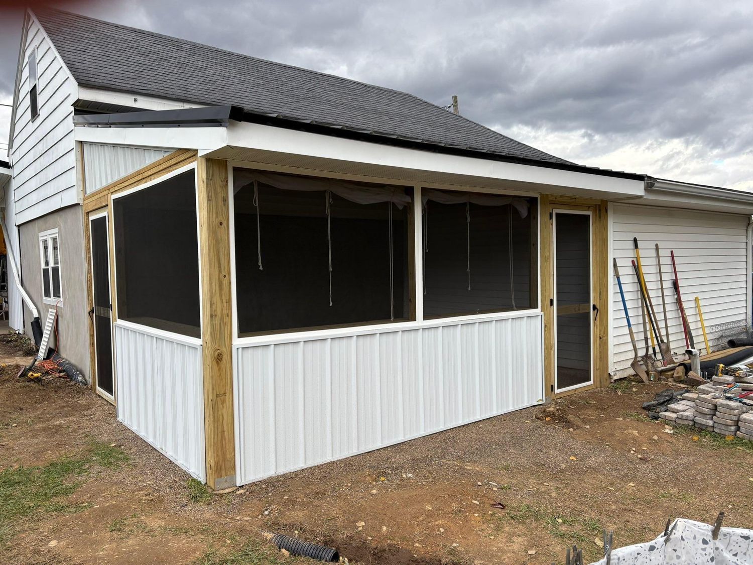 A side view of a house with a newly constructed, white-sided screened-in porch featuring exposed wood support beams.