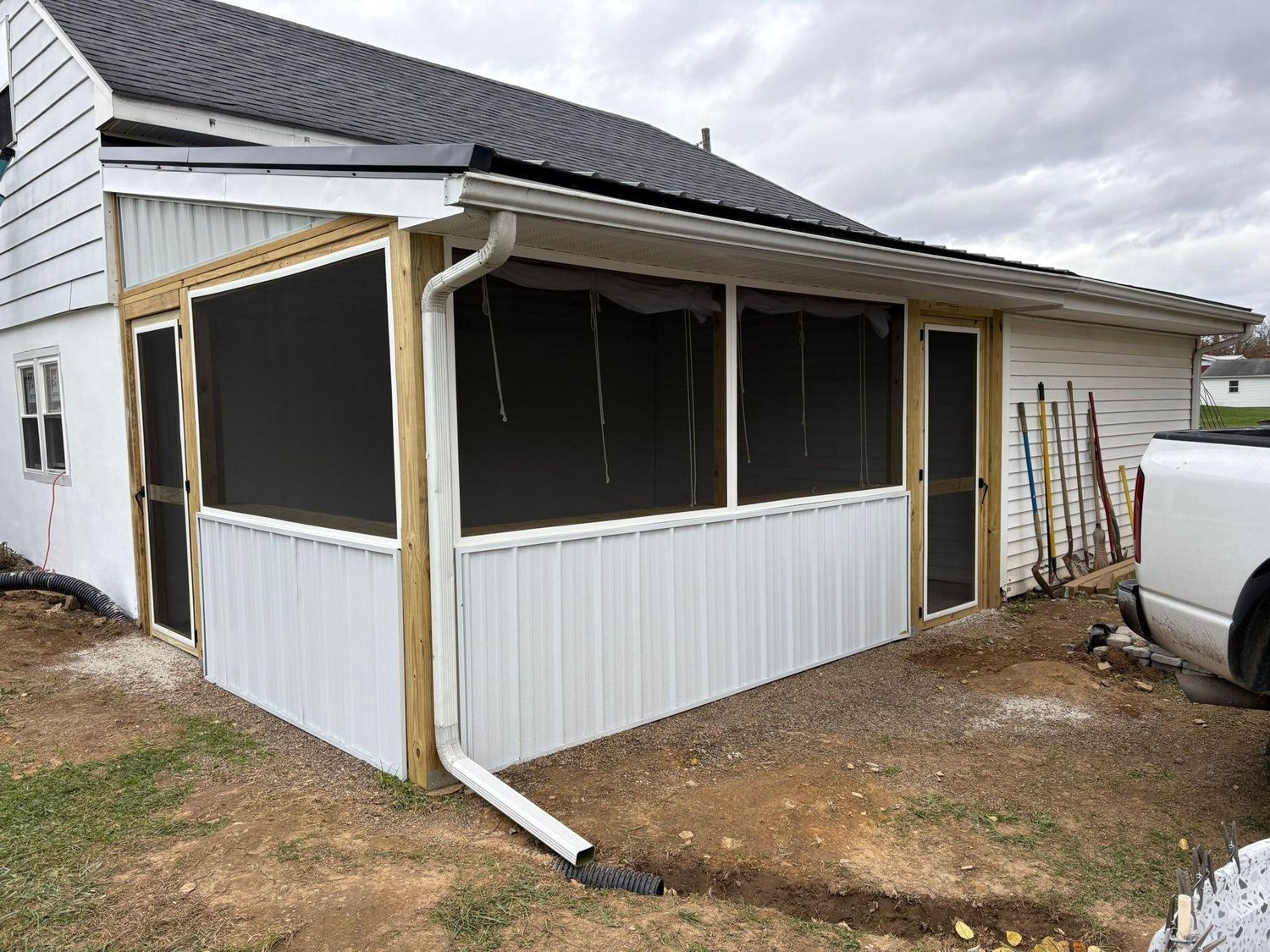 A white house featuring a newly constructed screened-in porch with wood framing, white vertical siding, and a downspout.