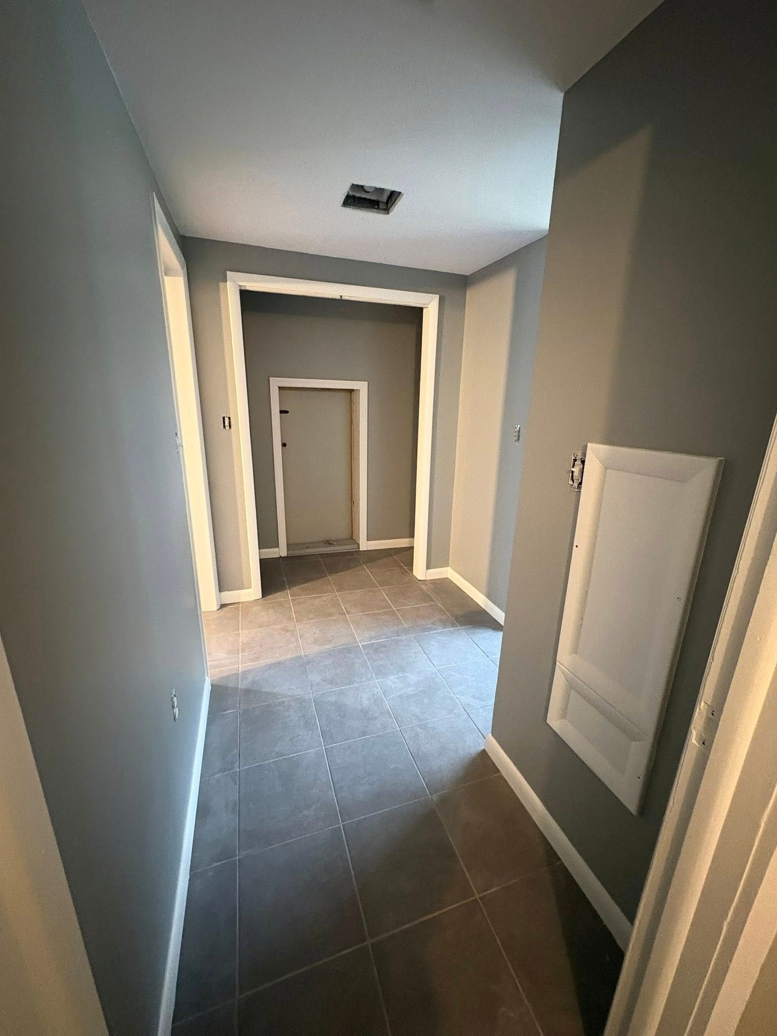 A hallway with gray walls, dark tiled floor, and two doorways of different sizes in the background.
