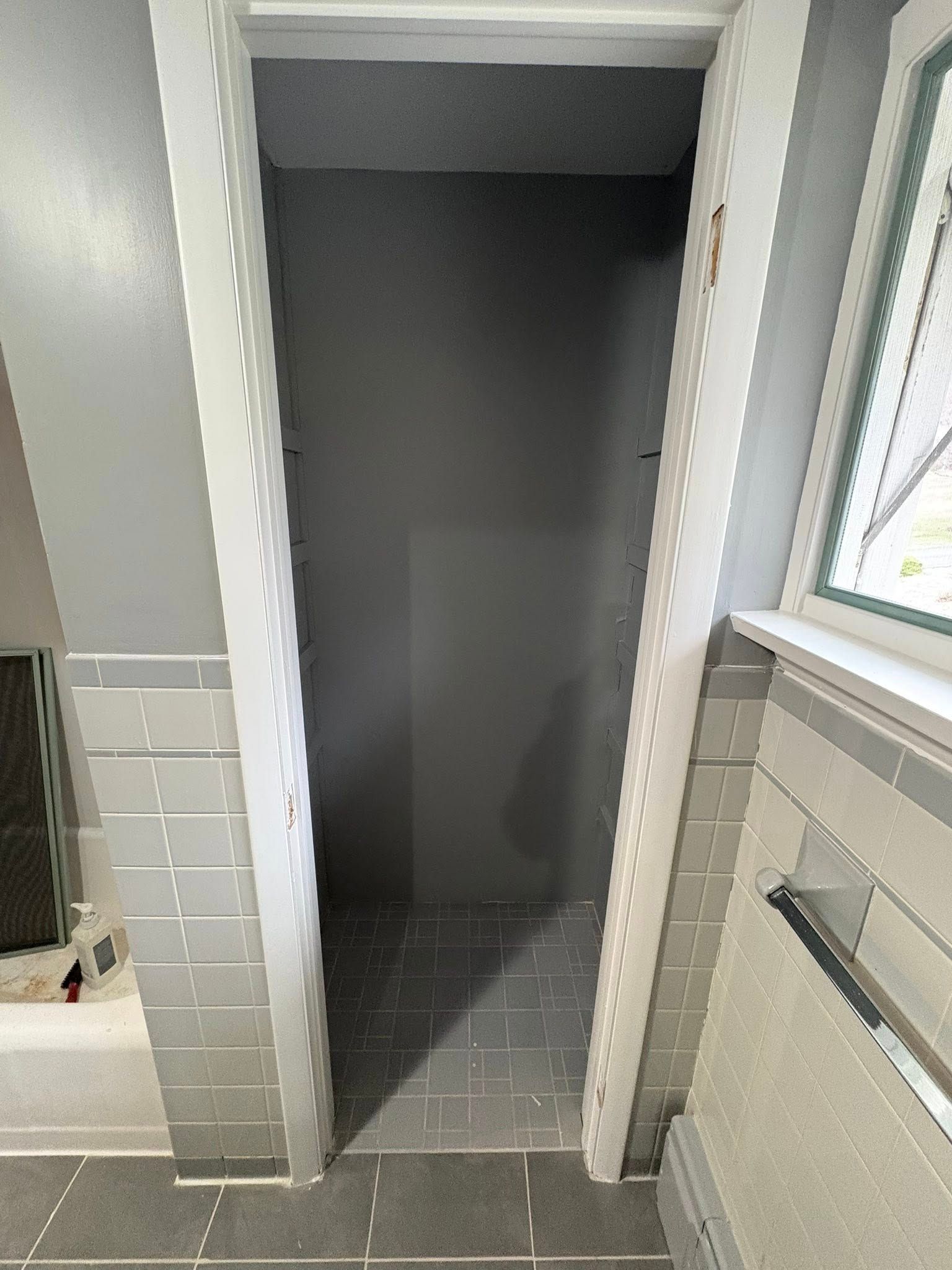 A narrow, empty doorway leading into a gray-walled closet or small room, positioned next to gray tiled walls and flooring.