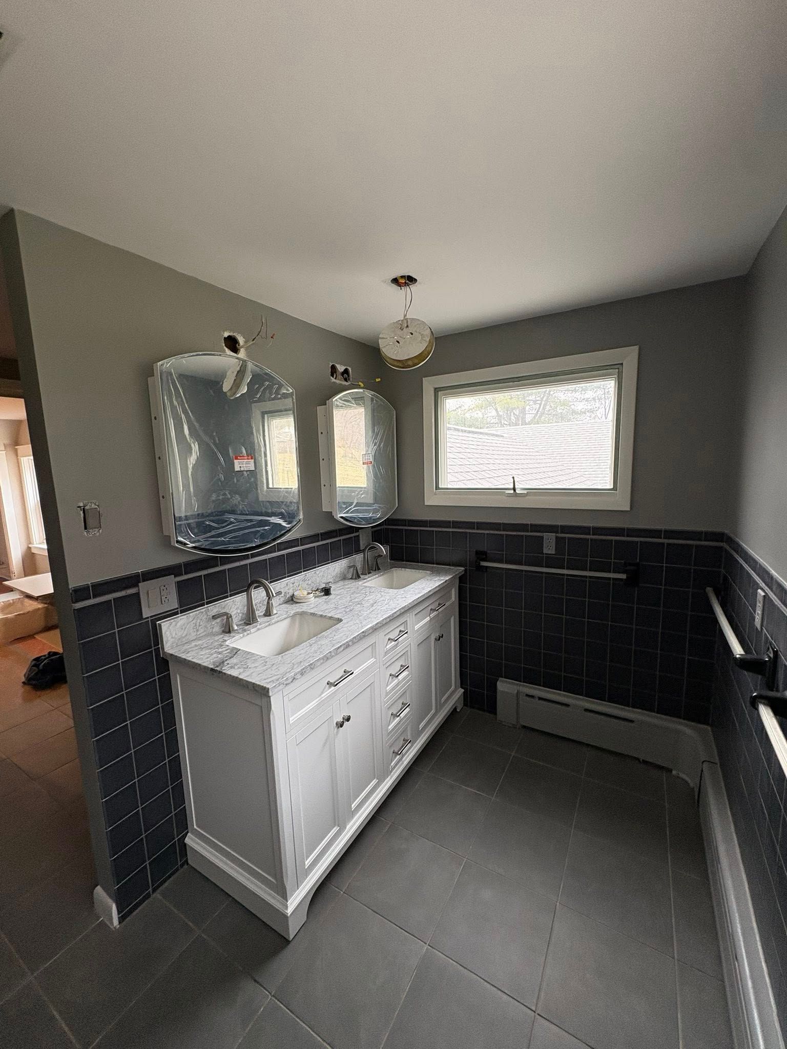 A small bathroom with light gray walls, a white vanity, a dark wood medicine cabinet, a window, and a toilet.