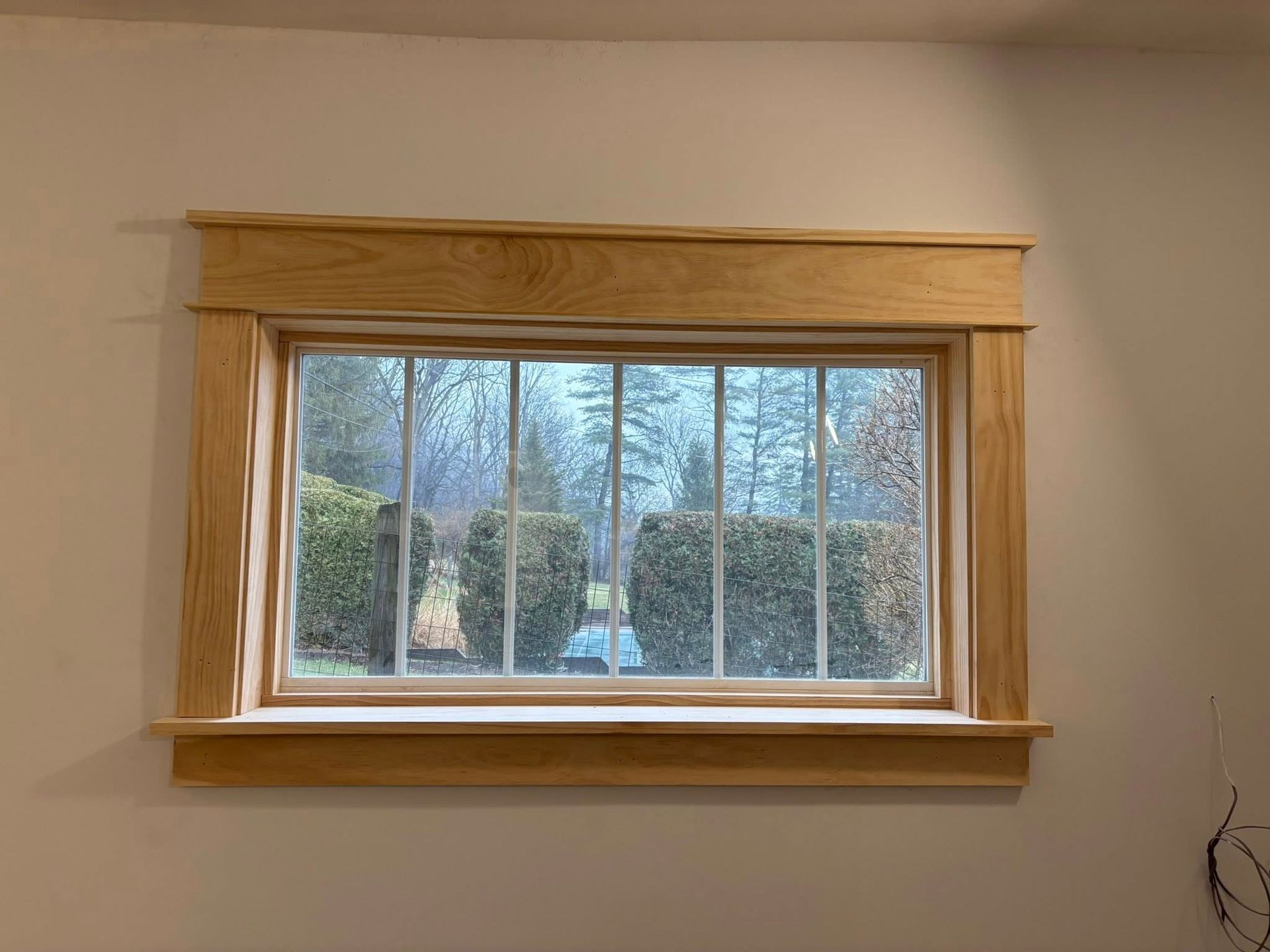A rectangular window with natural-colored wood casing, including a prominent header and sill, set against a plain wall.