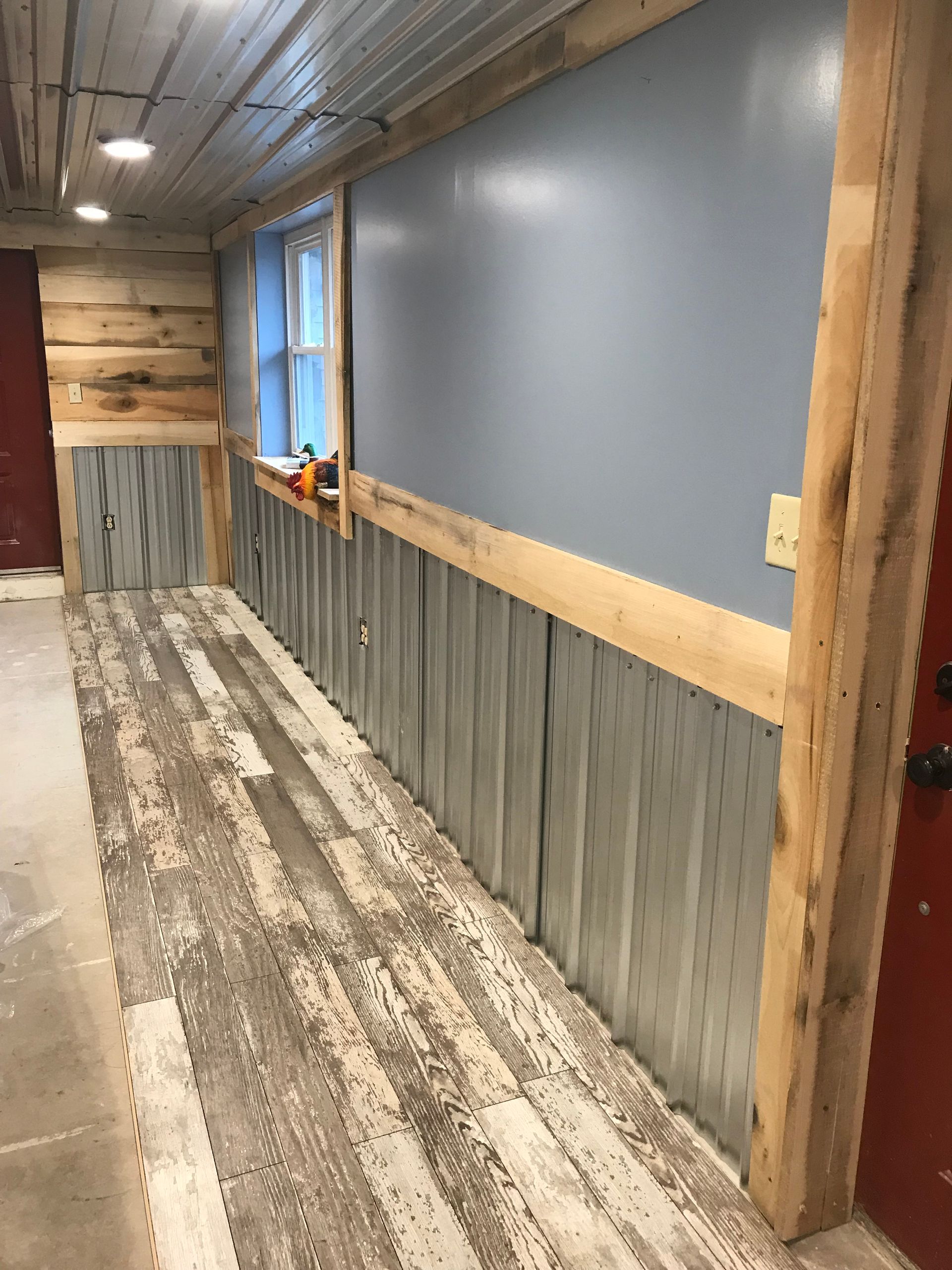 A hallway interior with metal corrugated wainscoting, light blue upper walls, wood trim, and rustic wood-look flooring.