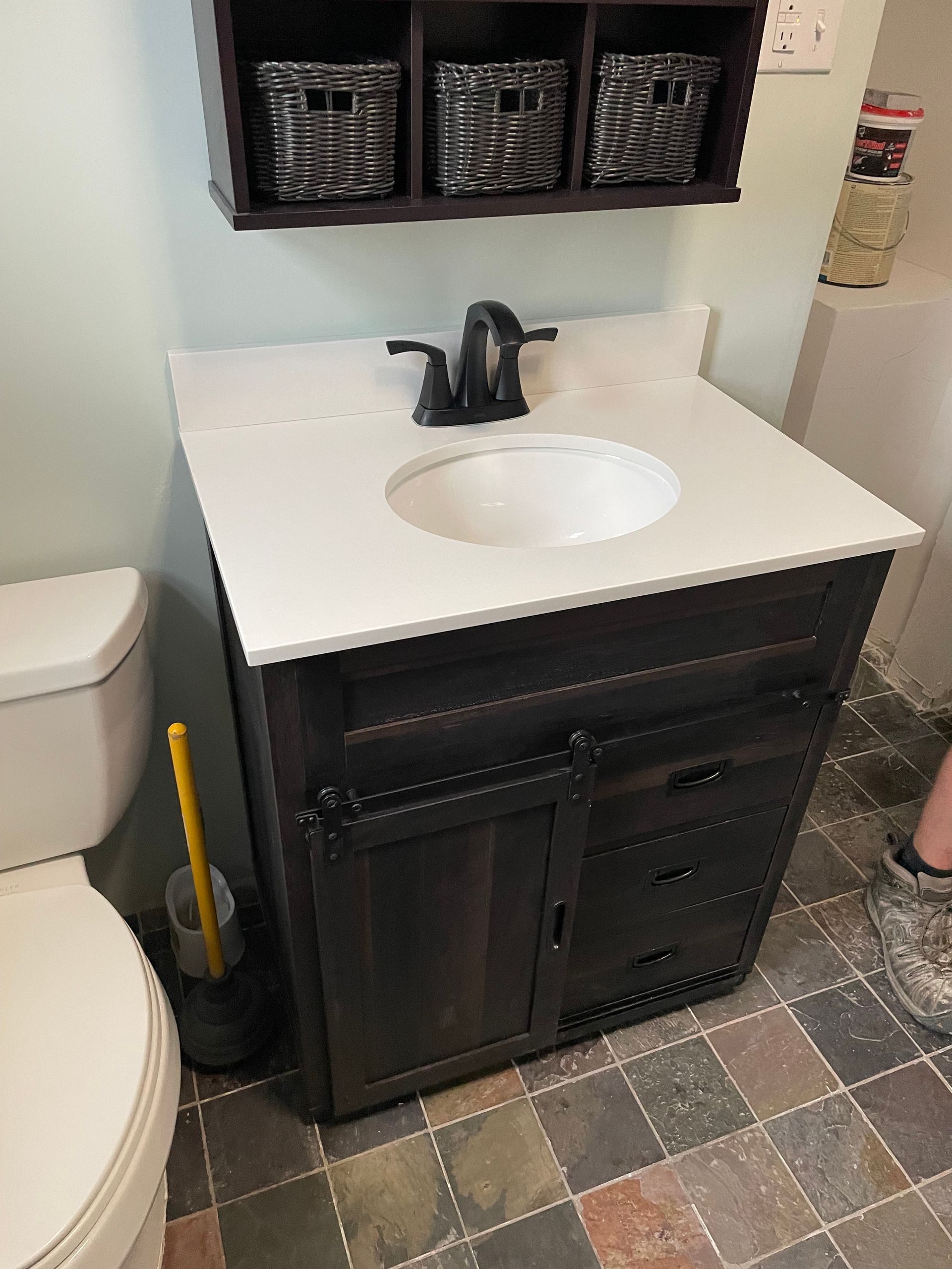 A dark wood vanity with a white countertop and sink, featuring three storage baskets on a wall shelf above it.