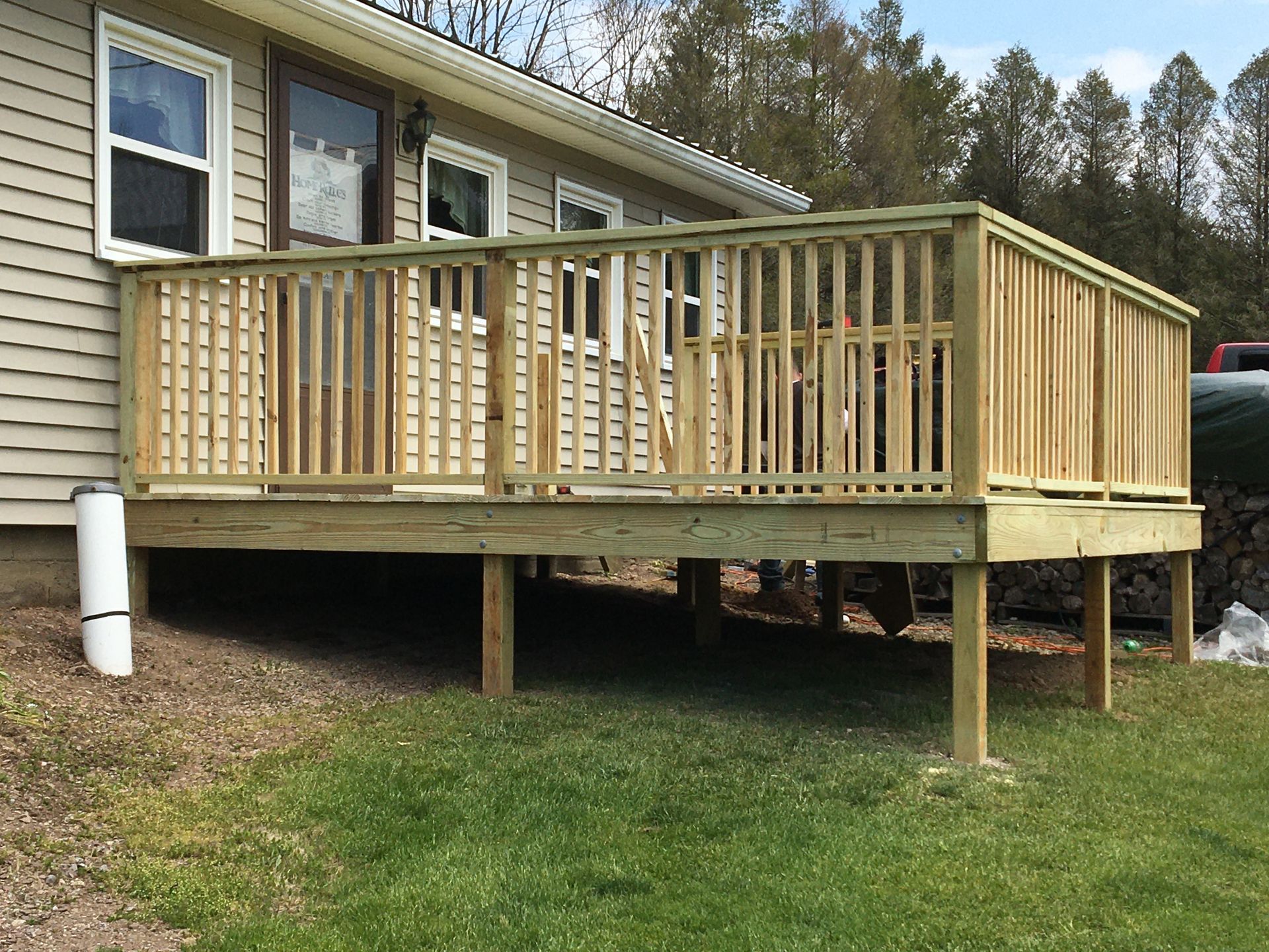 A newly constructed wooden deck with railings attached to the side of a light-colored house with tan vinyl siding.