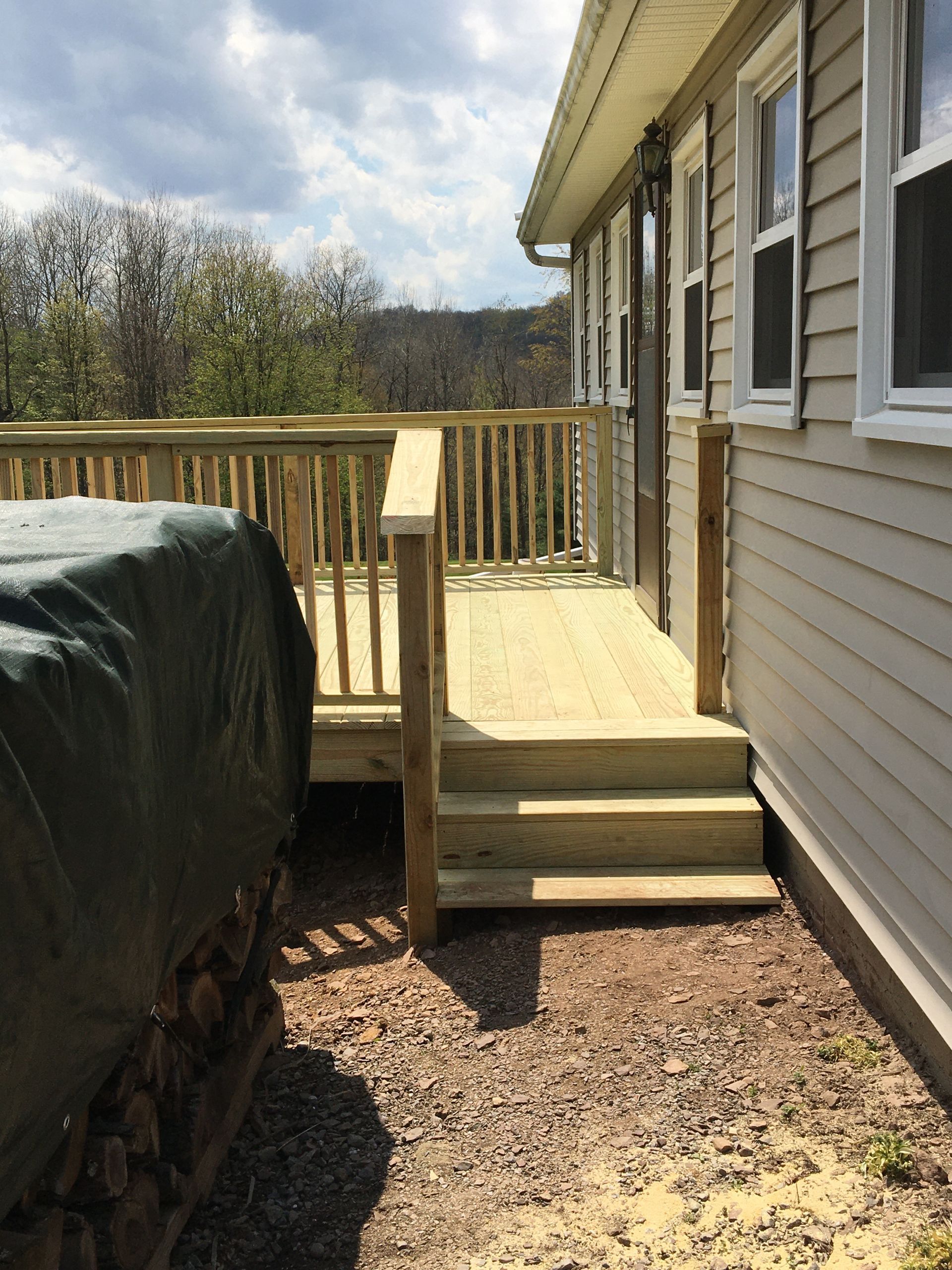 New wooden deck and steps attached to the side of a light-colored house overlooking a wooded area.