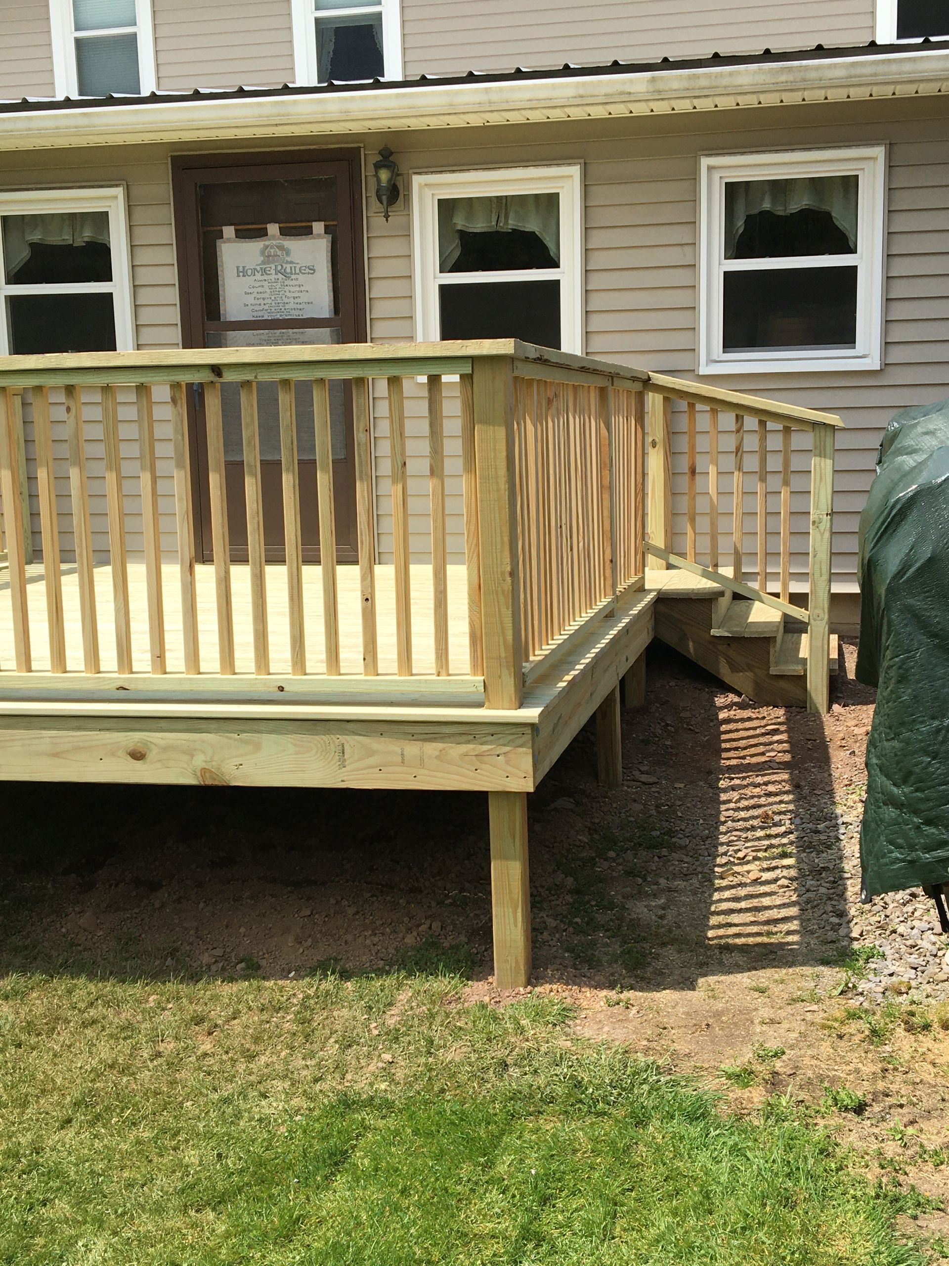 A newly constructed wooden deck attached to the side of a house, featuring stairs leading down to a gravel area.