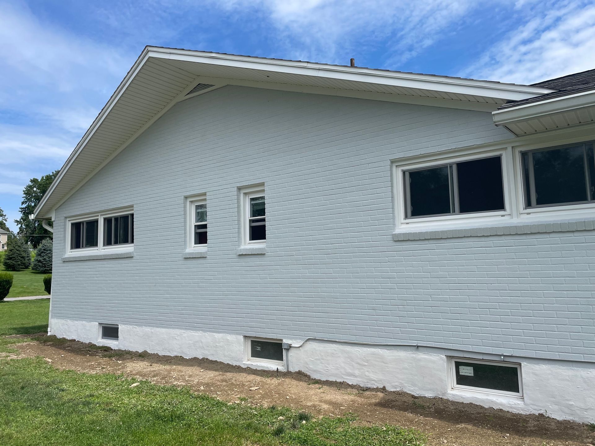 Side view of a house with light grey vinyl siding, a white foundation, several windows, and a grassy yard.