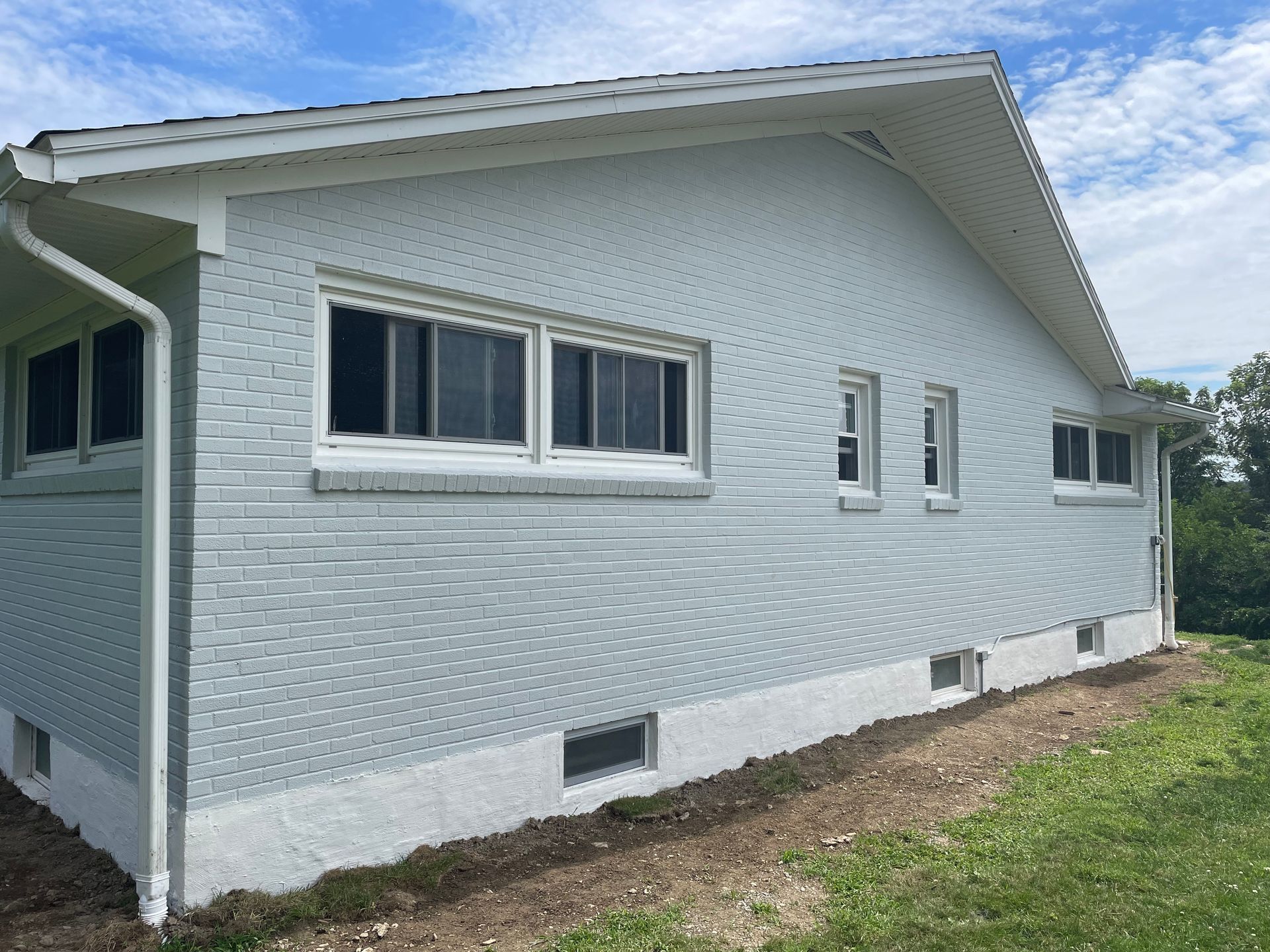 Side view of a house with light grey painted brick siding, white window trim, and a white concrete foundation.