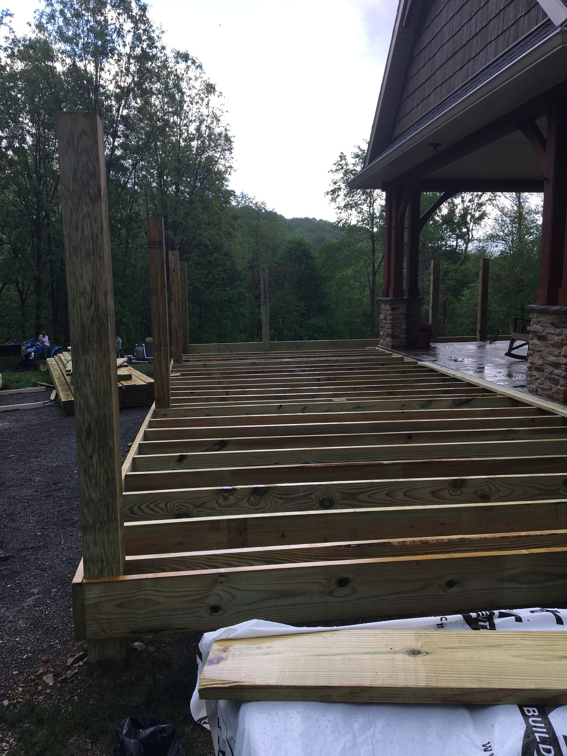 A wooden deck frame under construction with vertical posts installed, situated outdoors beside a house.