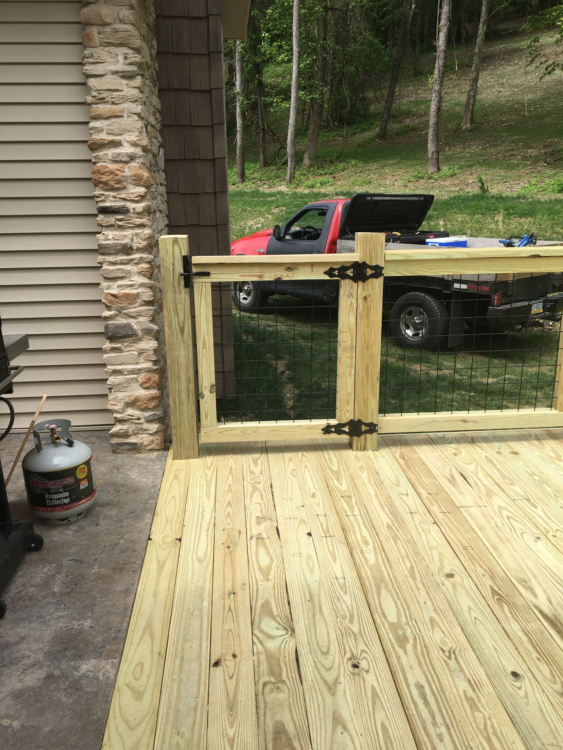 A wooden deck gate attached to a house wall and a post, with a pickup truck parked in the background.