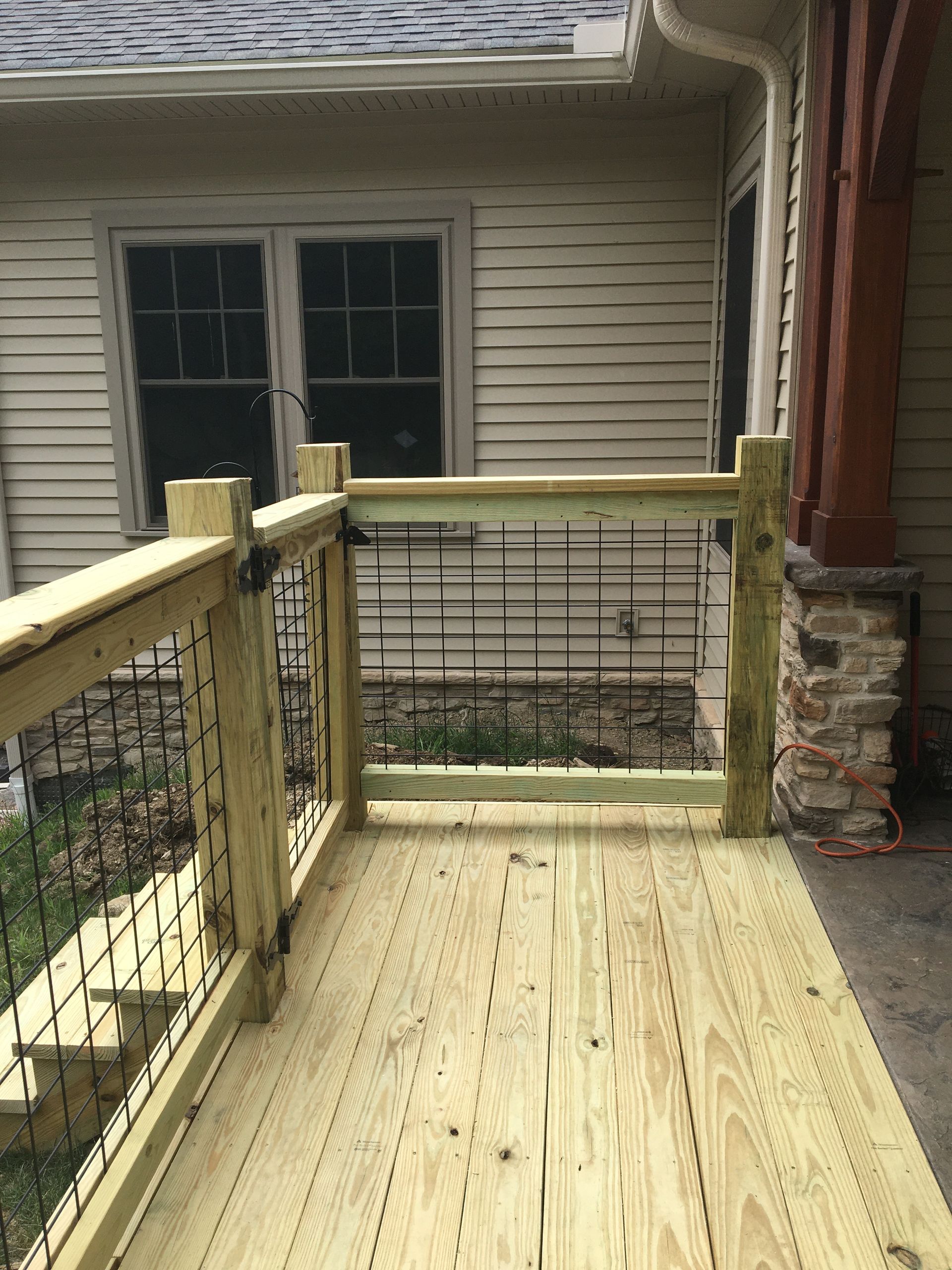 Newly installed light-colored wooden deck railing with black metal mesh infill panels against a house exterior.