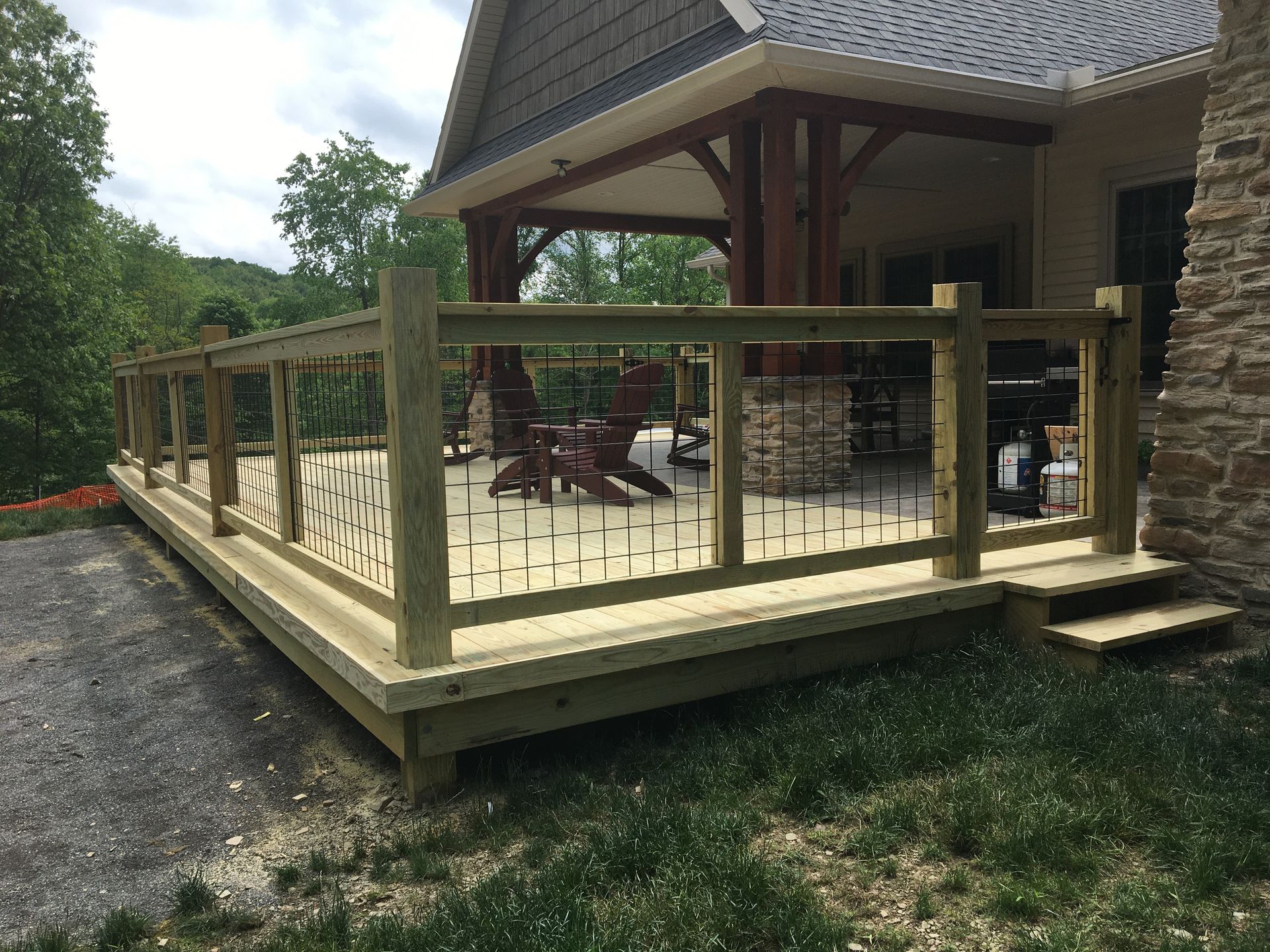 A wooden deck with railing and metal spindles sits beside a stone-accented house with a covered patio and rocking chairs.
