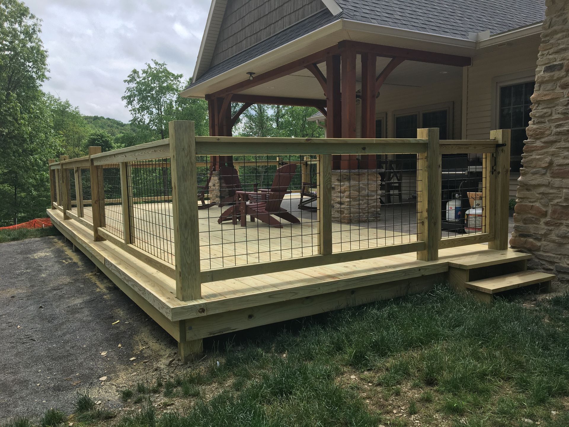 A wooden deck with metal balusters attached to a stone house, featuring an outdoor seating area under a covered porch.