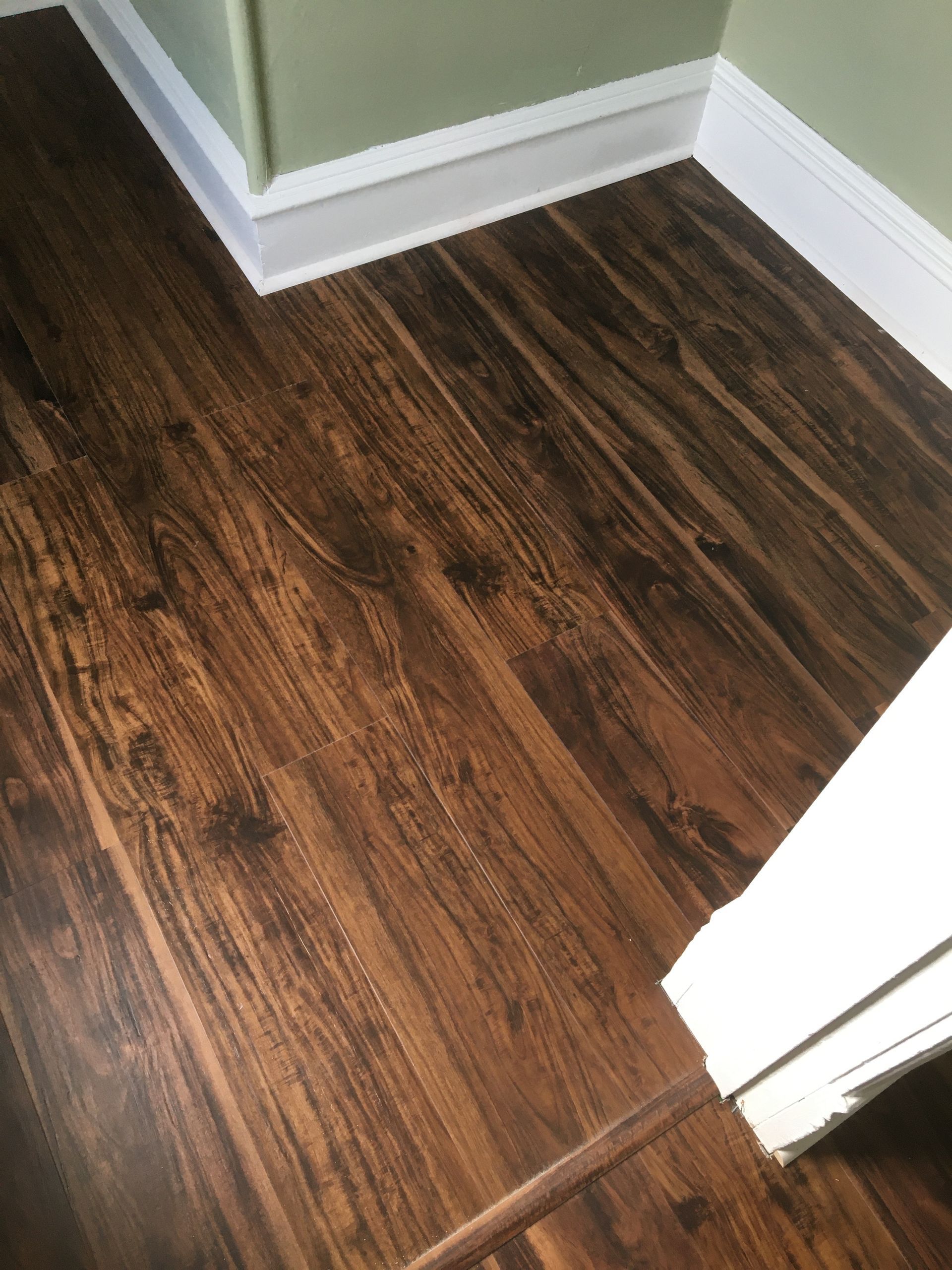 Dark wood-look flooring meeting white baseboards and a doorway corner in a room with light green walls.