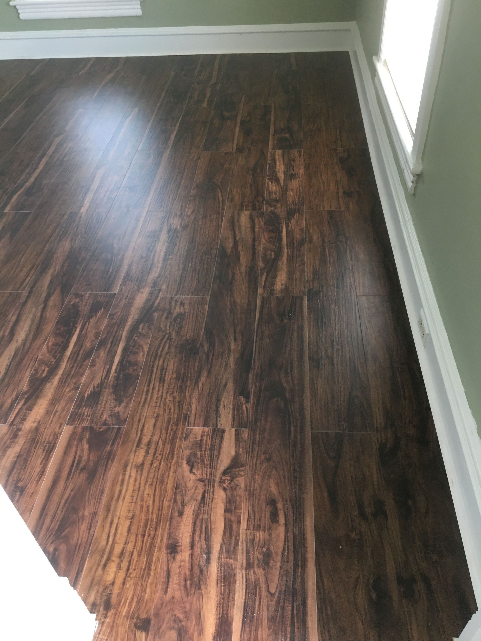 Dark wood-look laminate flooring installed in a room with light green walls and white baseboards.