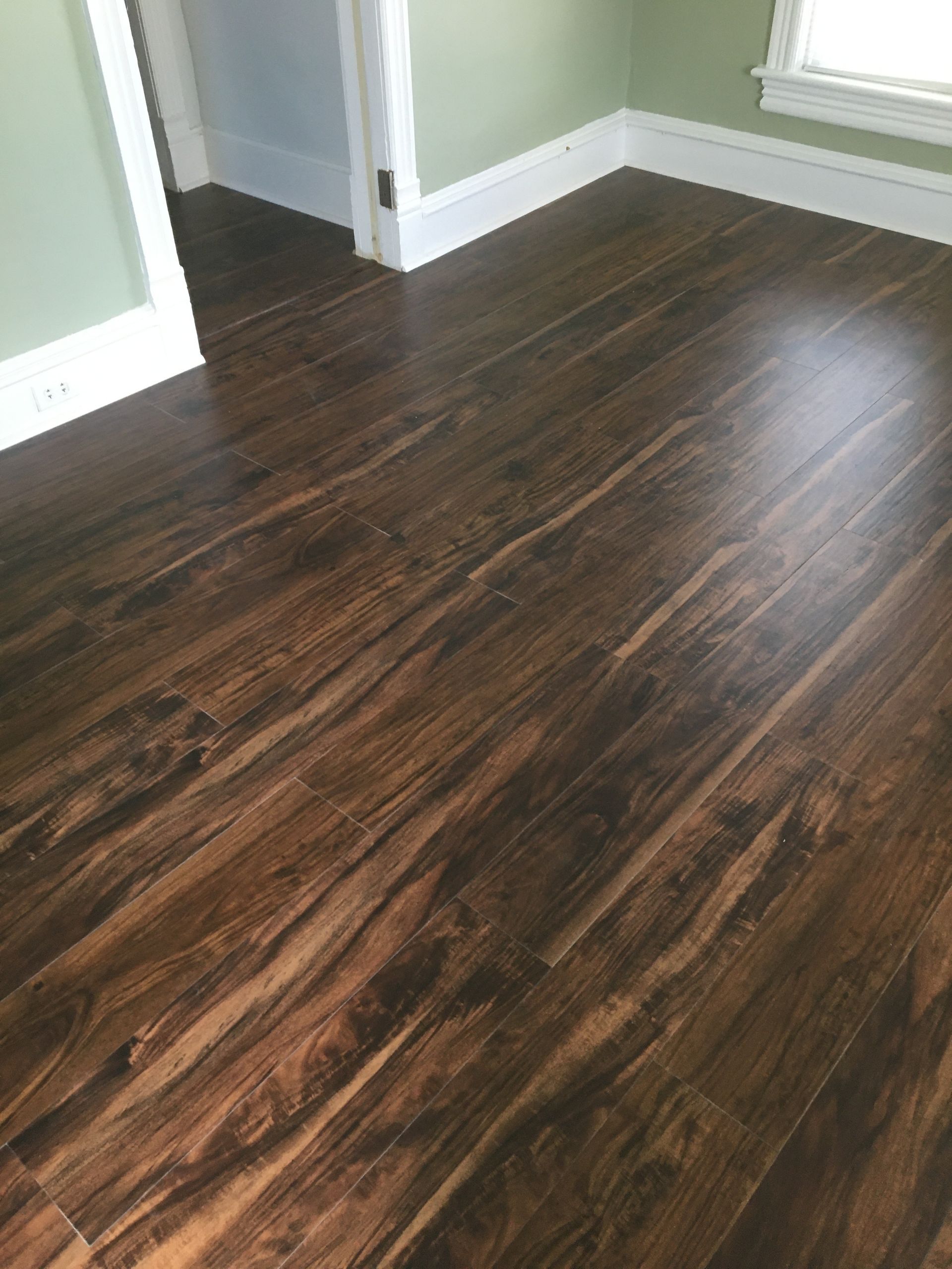 Dark brown wood laminate flooring with visible grain patterns in a room with light green walls and white trim.