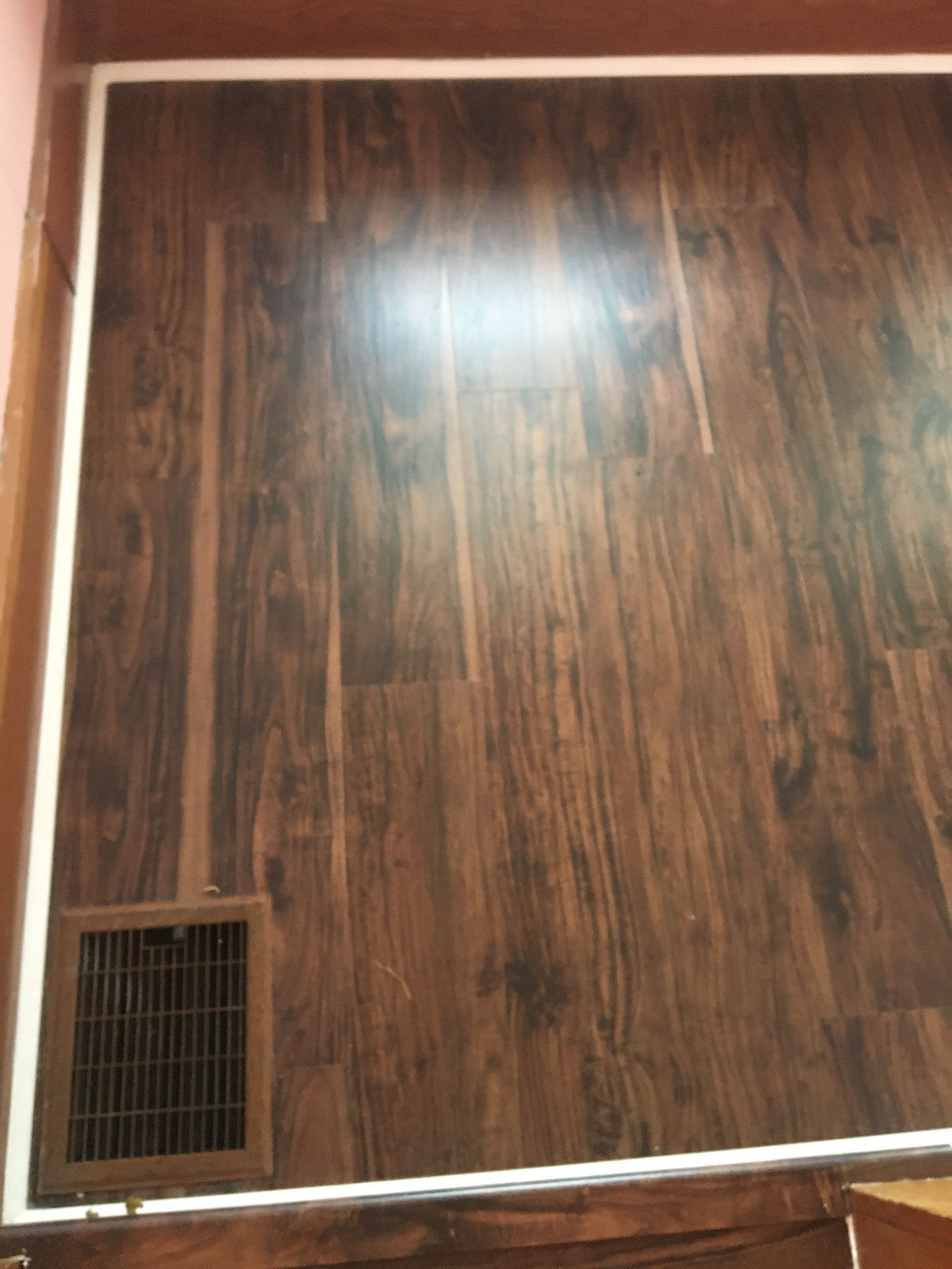 A dark wood-look floor with a rectangular vent cover in the corner, bordered by a white trim.