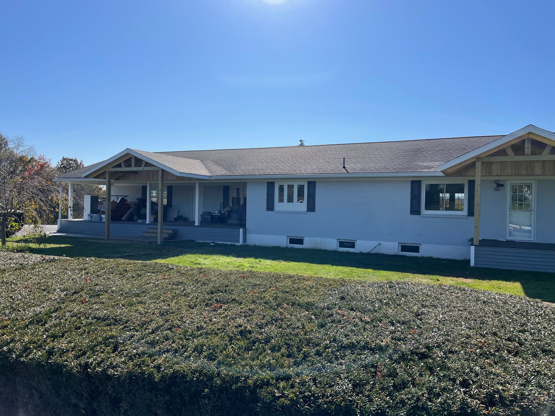 A gray, one-story house with a wooden front porch and covered side patio under a clear, bright blue sky.