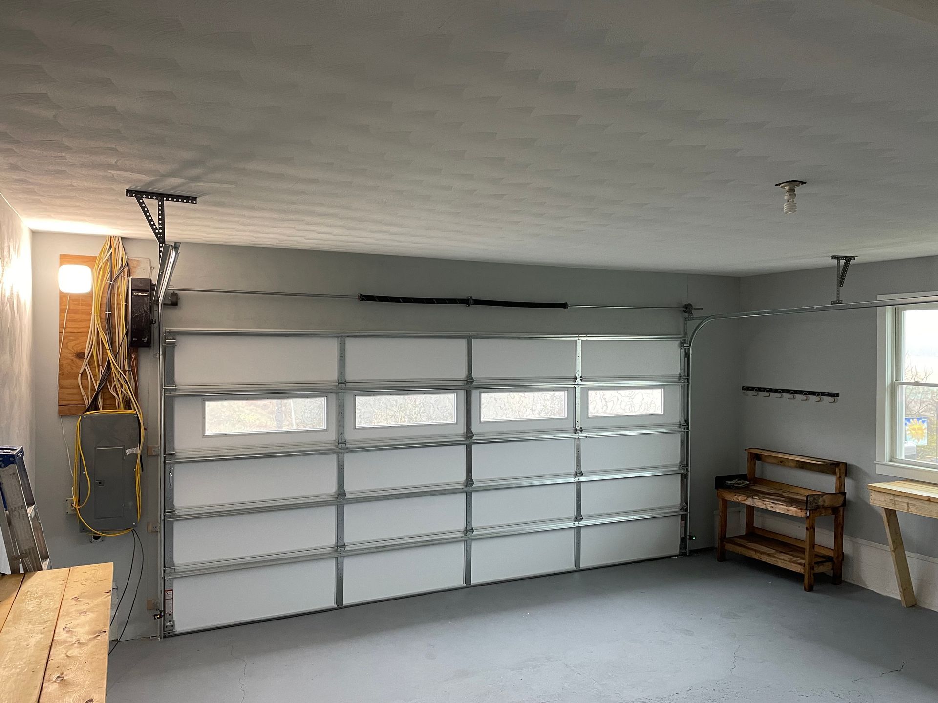 A modern garage interior with a closed white sectional door, gray walls, and a wooden bench along the side wall.