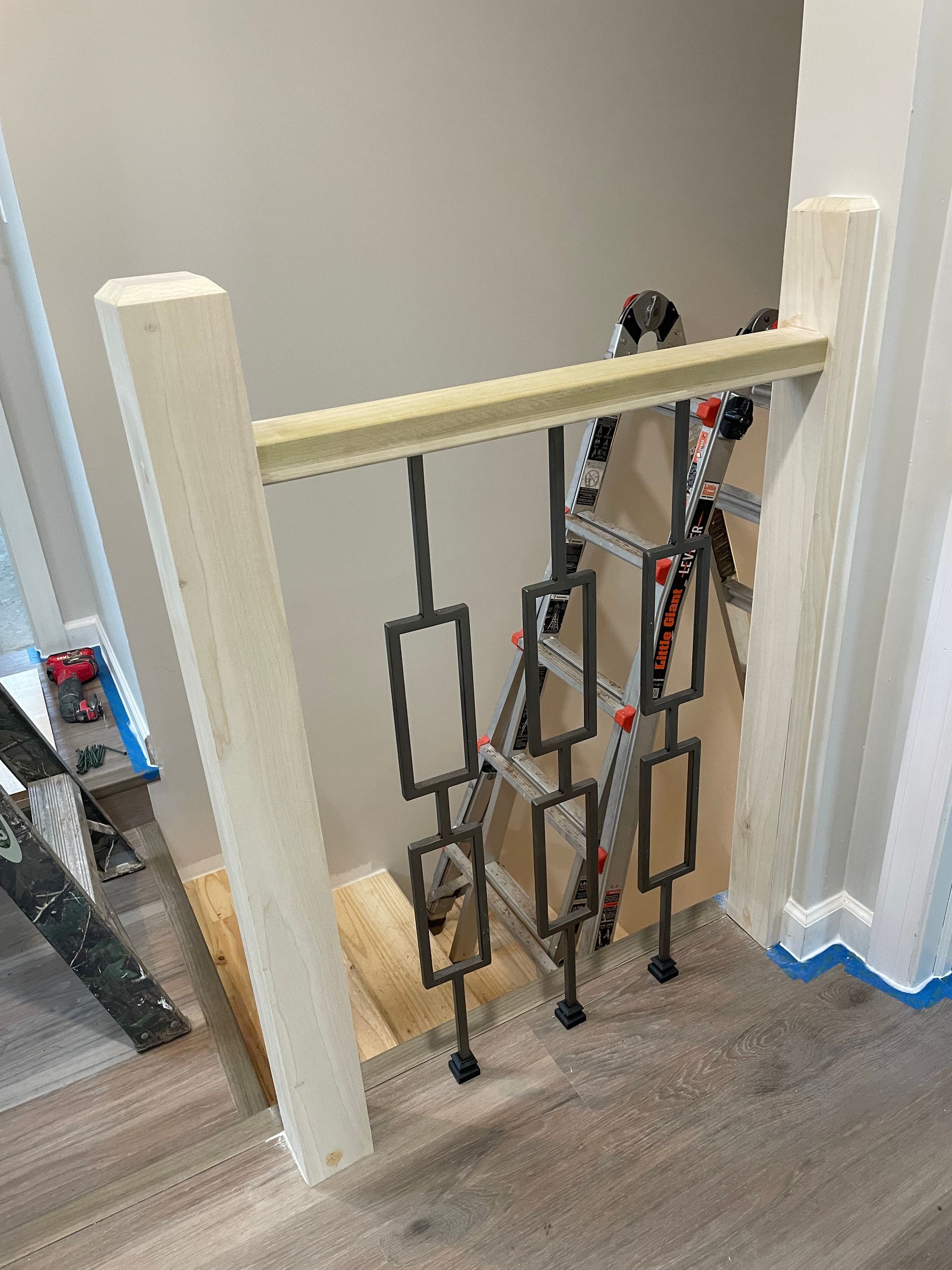 A stair railing under construction, featuring vertical metal balusters with rectangular patterns between two wooden posts.