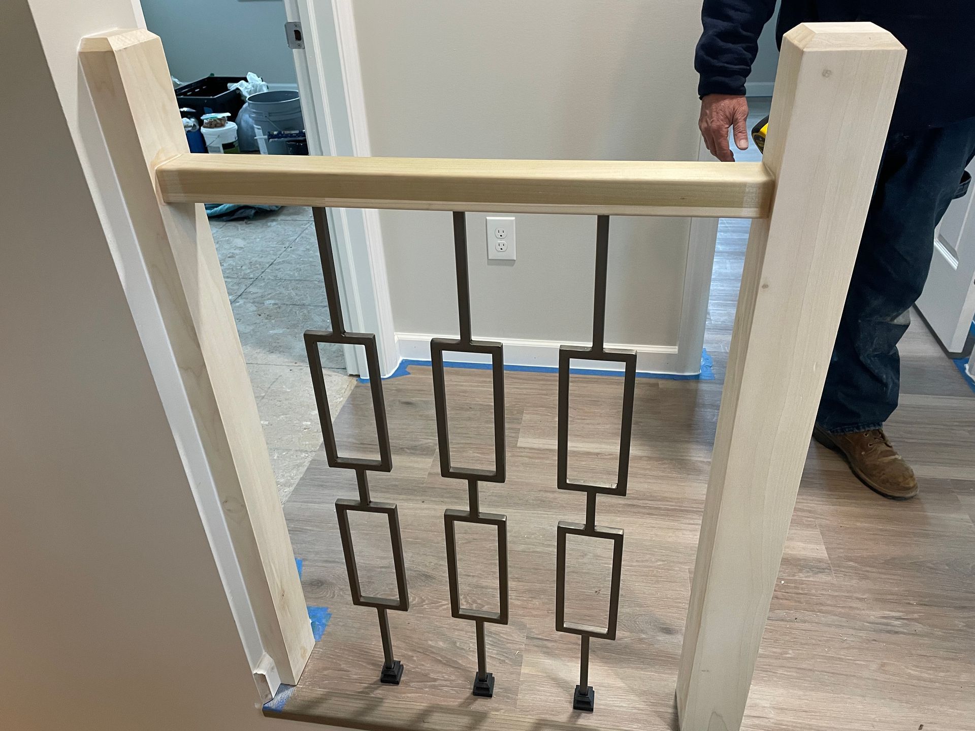 A newly installed wooden stair railing with three decorative bronze-colored metal geometric balusters in a hallway.