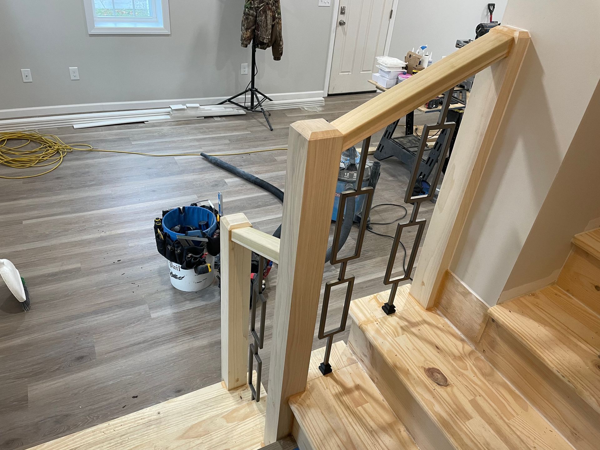 New wooden staircase railing with metal balusters under construction in a room with grey flooring and tools.