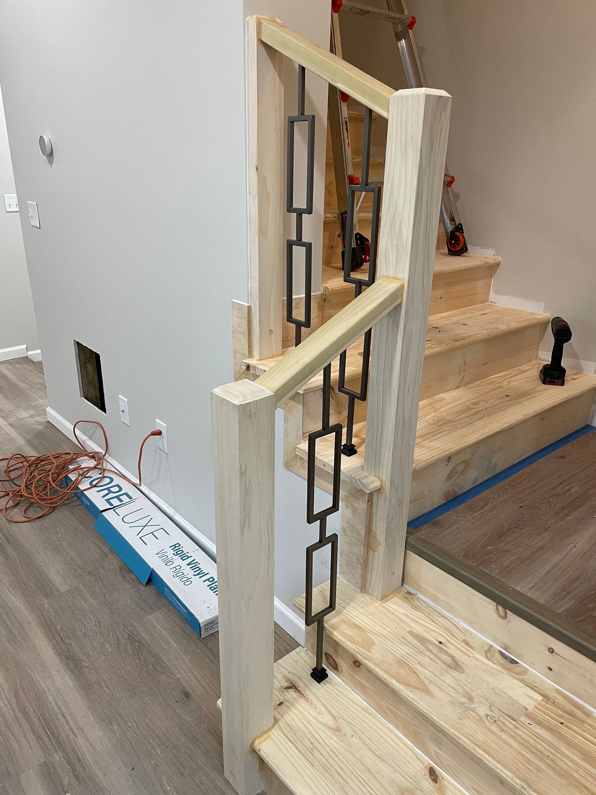 Construction of a wooden staircase railing with decorative black metal rectangular spindles in an unfinished interior.