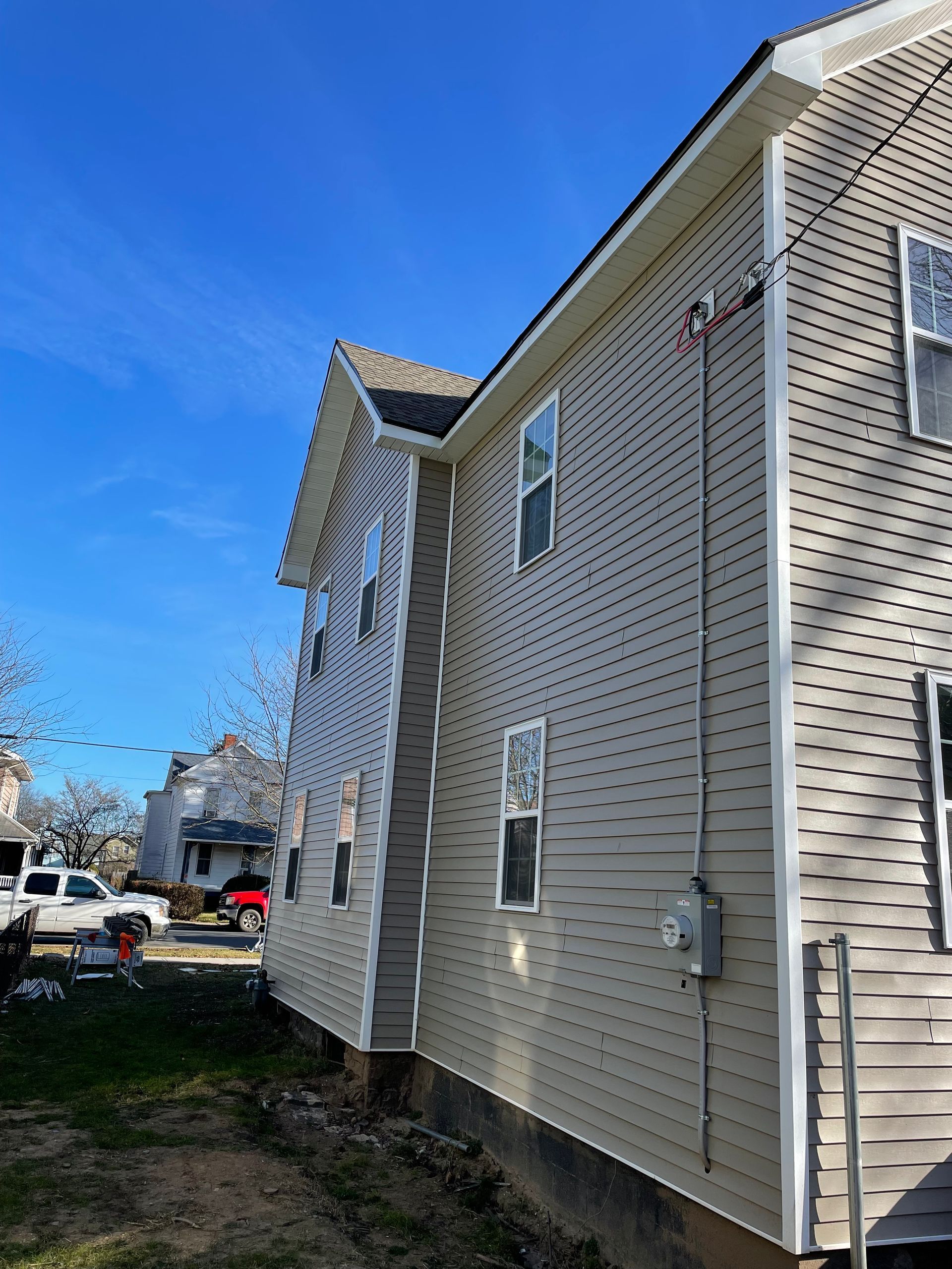 Side view of a light-tan house with white trim, featuring several windows and an exterior electrical meter.