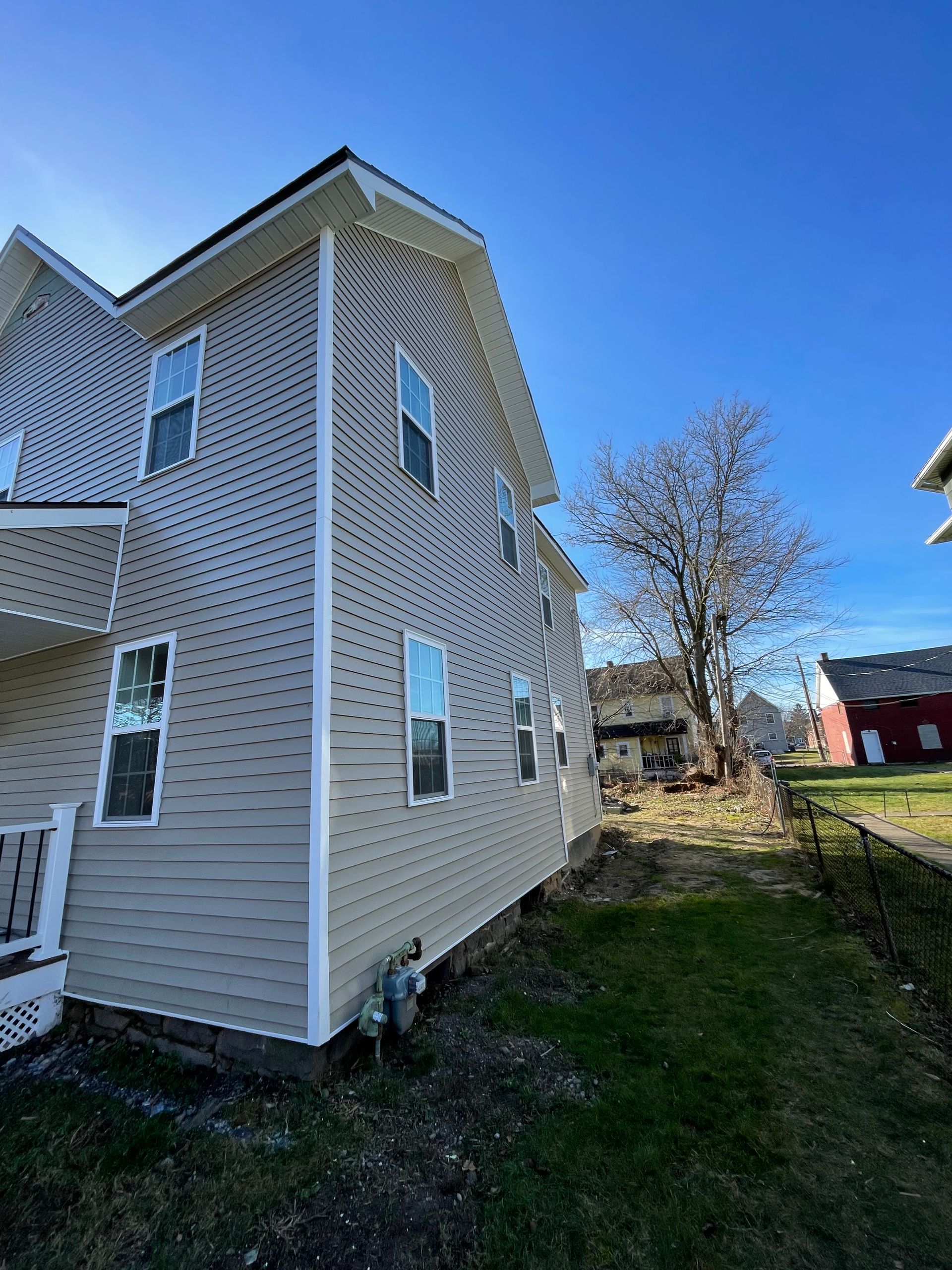 A low-angle view of a beige, two-story vinyl-sided house with white trim under a clear blue sky.