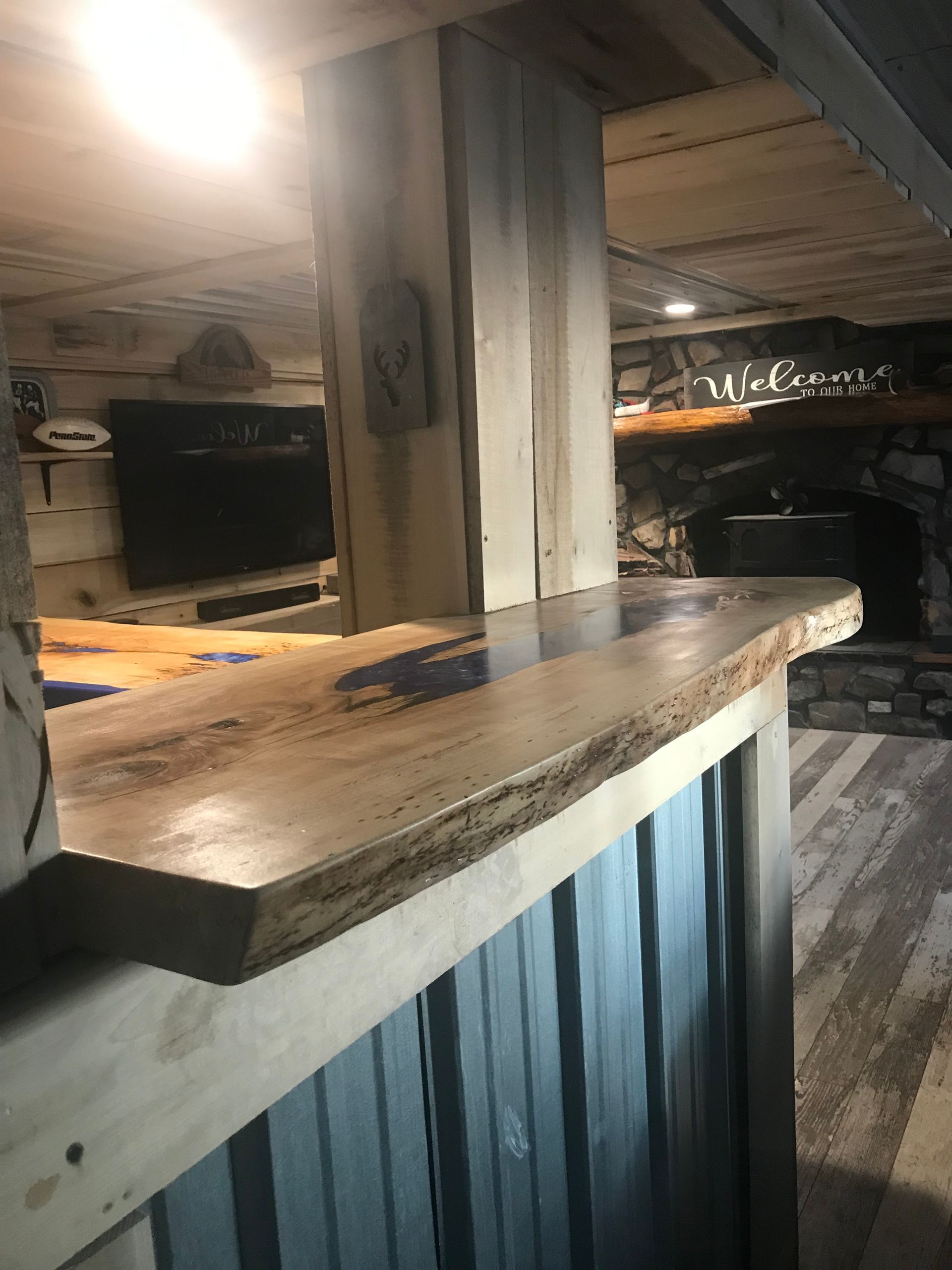 A rustic bar counter with a live-edge wooden top and blue resin inlay, set in a cozy room with a stone fireplace.