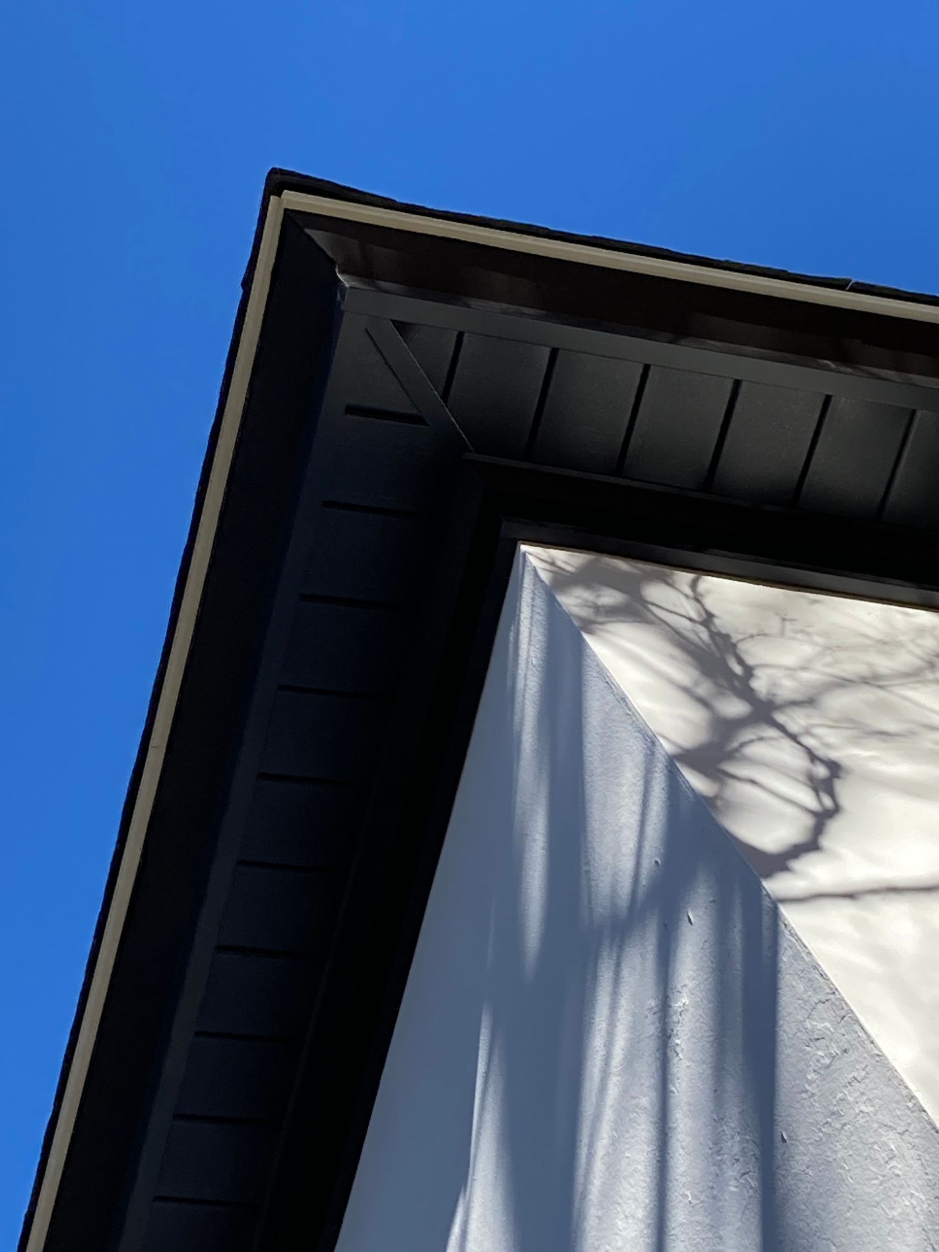 The corner of a roof with black eaves meeting a white wall against a clear blue sky.