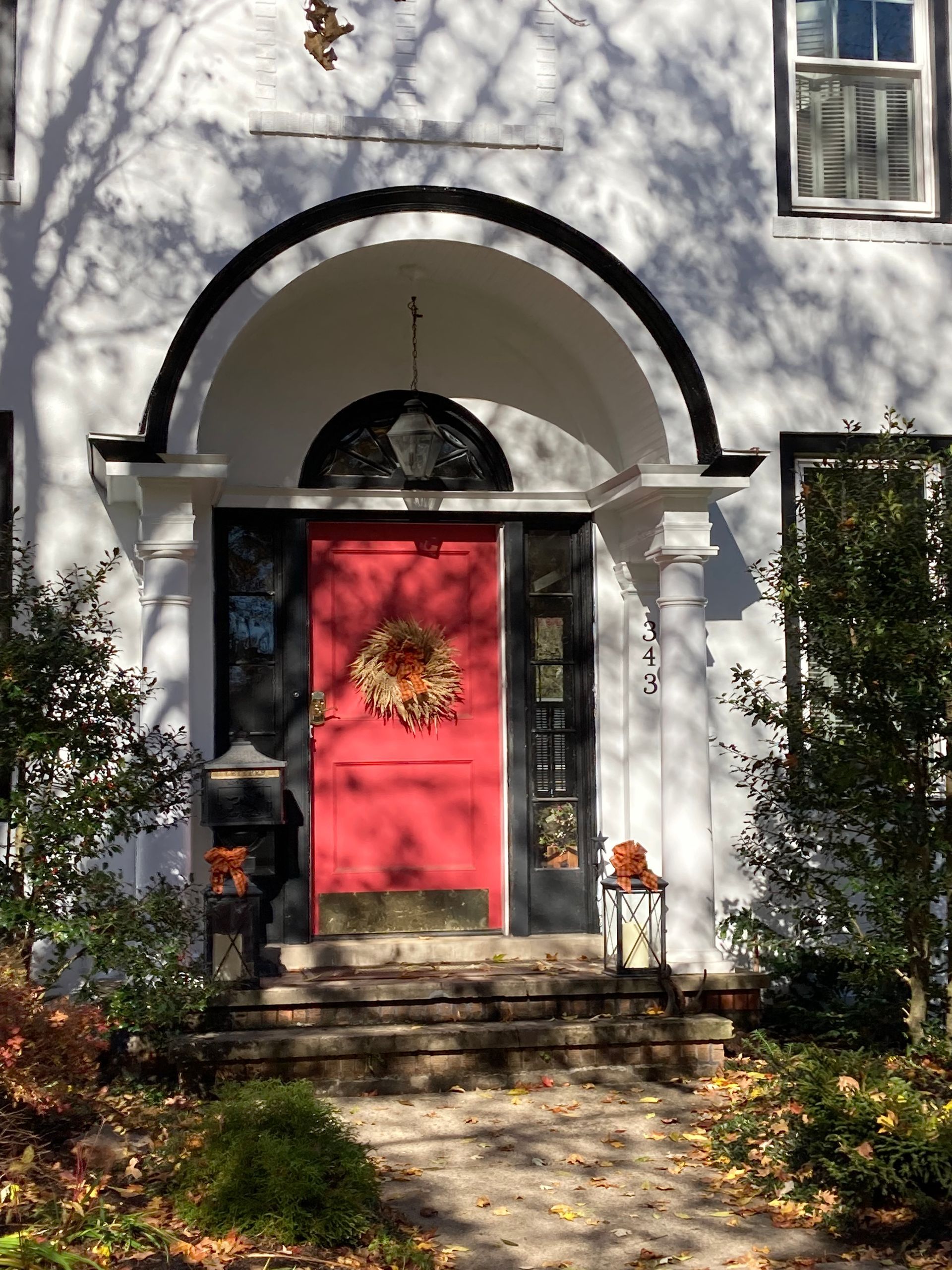 A bright red front door decorated with a wreath inside a white arched entryway with black trim and stone steps.