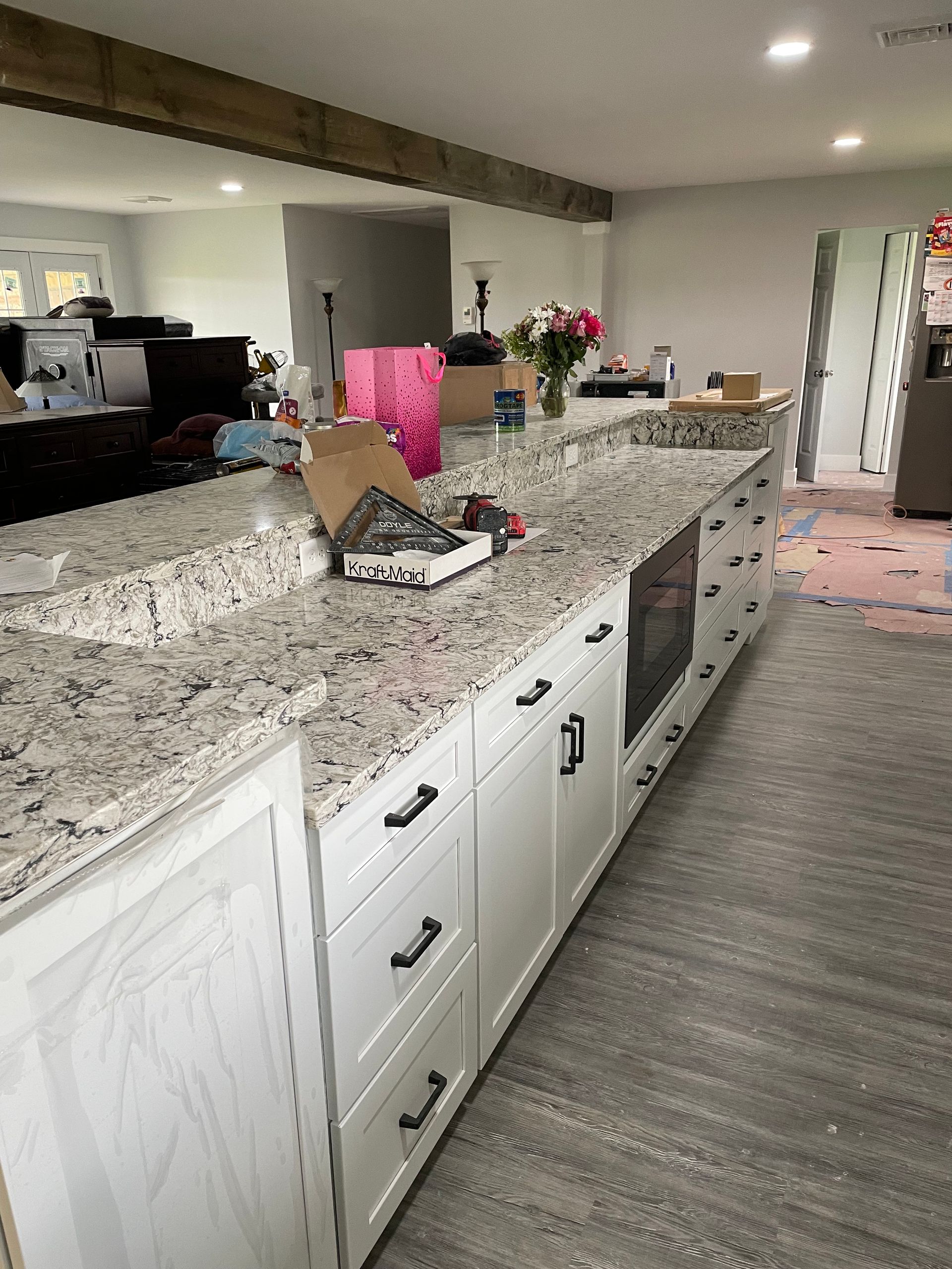 A kitchen island with a granite countertop and white cabinets, situated in a home with wood beams and gray flooring.