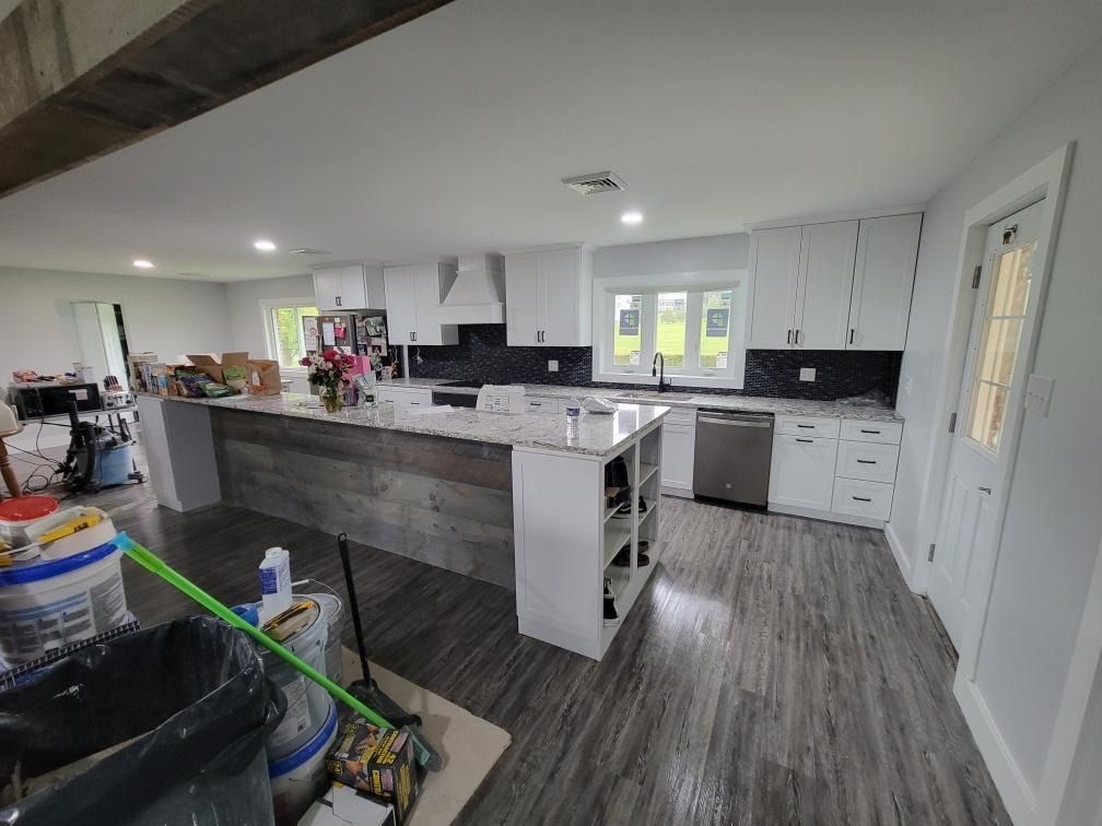 A modern kitchen with a wood-paneled island, white cabinets, grey flooring, and white countertops under construction.