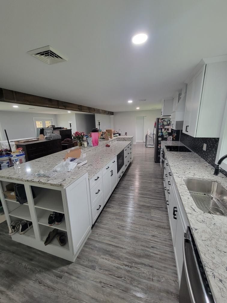 Modern kitchen featuring a long, white island with granite countertops, light gray wood-look flooring, and a sink.