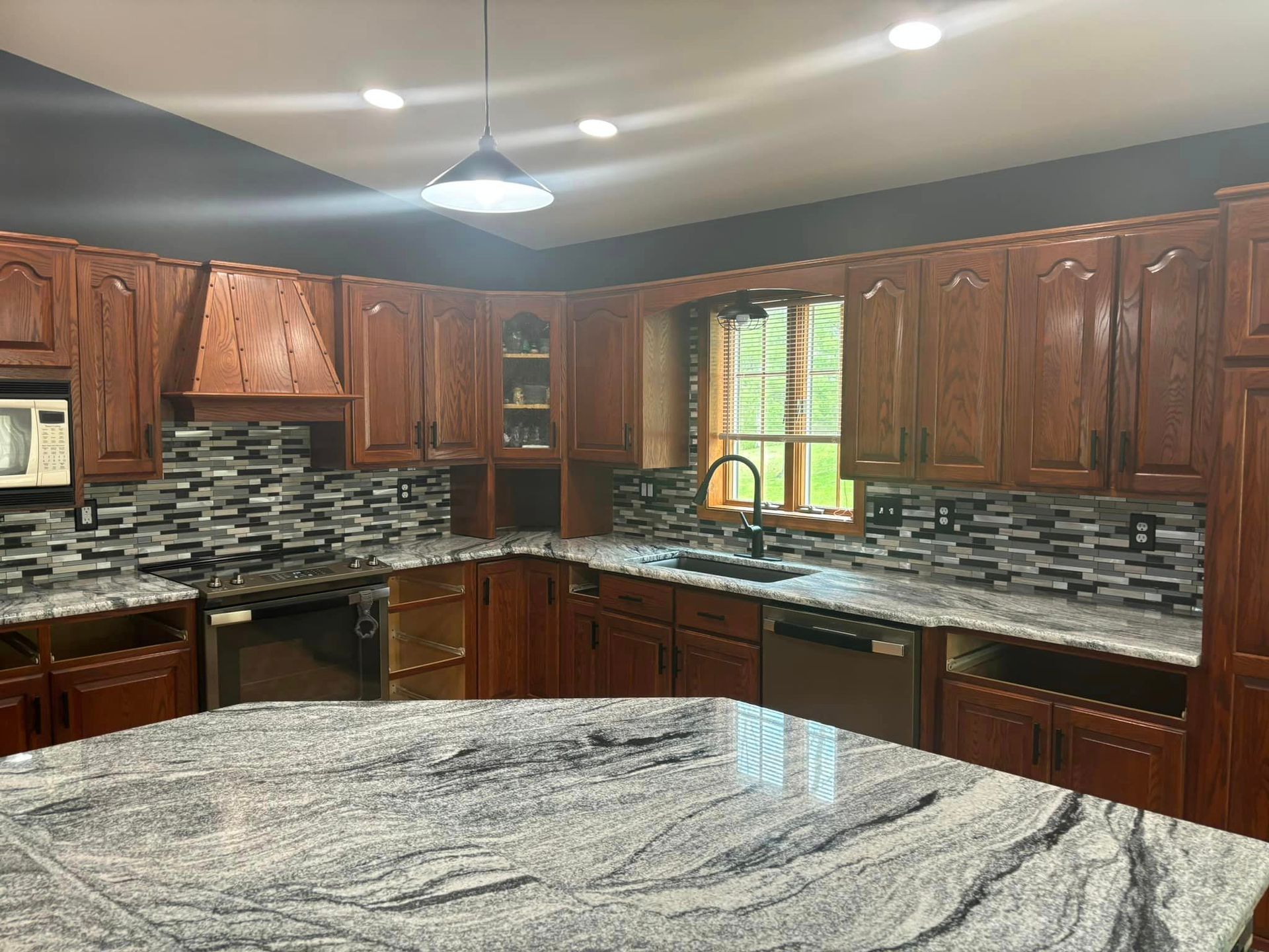 Kitchen with wood cabinets, granite countertops, a stone tile backsplash, a stainless steel stove, and an island.