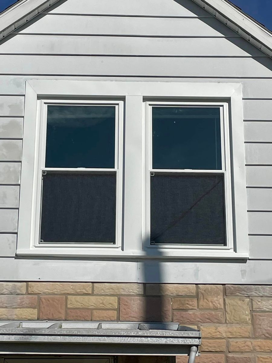 White double-pane window with dark screens set in a wall with white horizontal siding above brickwork.