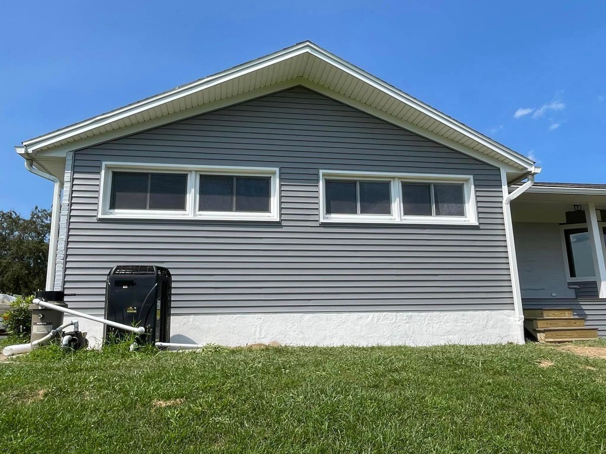 A gray-sided house with two horizontal windows and a white foundation under a blue sky.