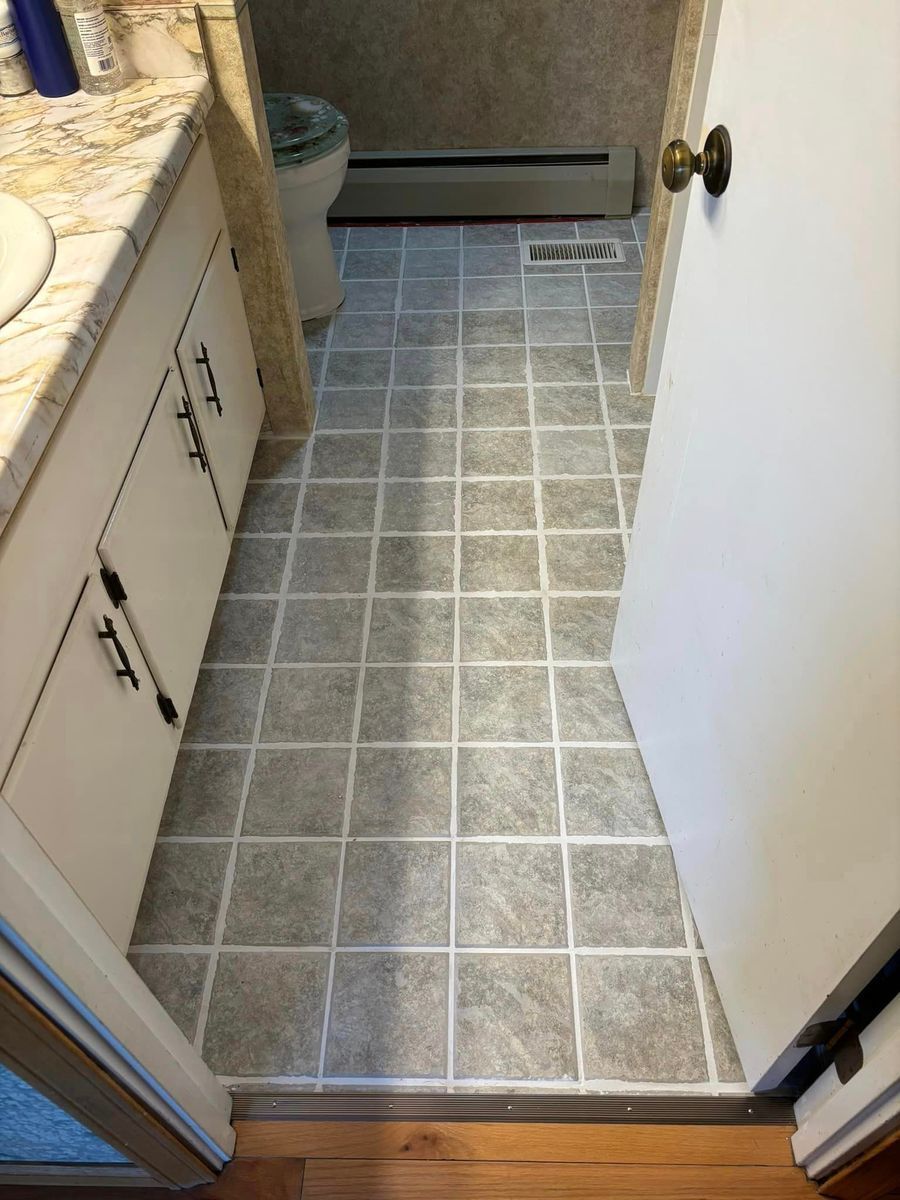 Bathroom entrance with gray and white tile flooring, a white vanity cabinet, and a door on the right.