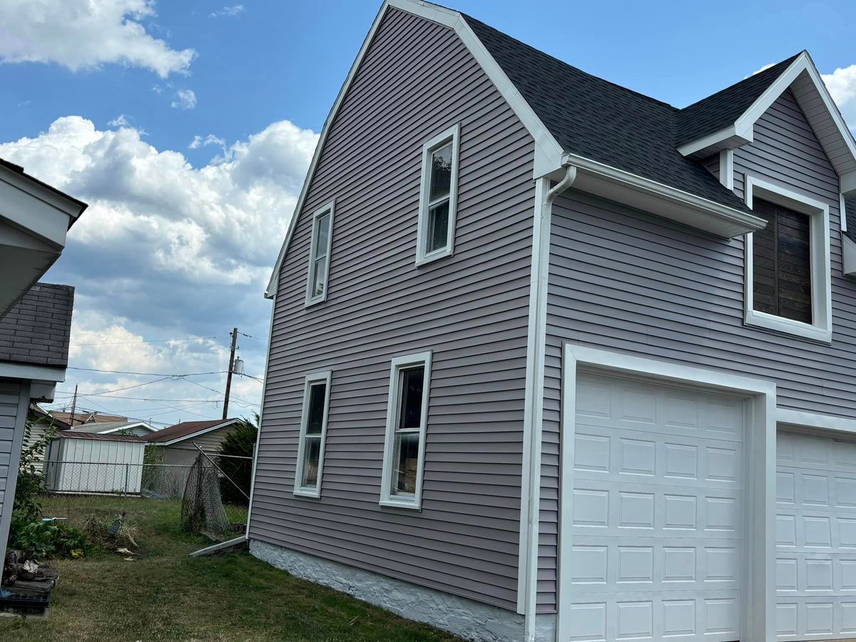 A two-story house with purple siding and a dual garage, set under a blue sky with white clouds.