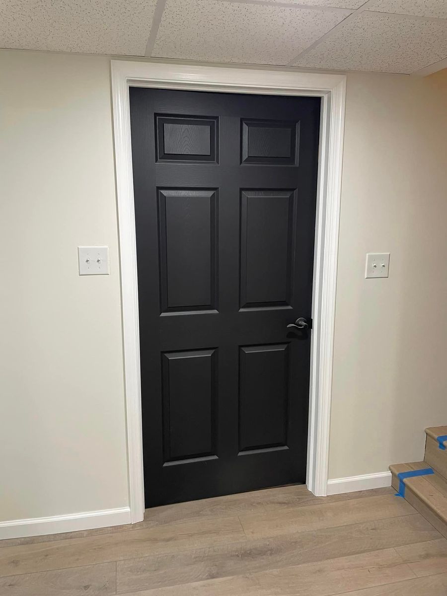 A black six-panel door framed in white trim, centered on a light-colored wall above a wooden floor.