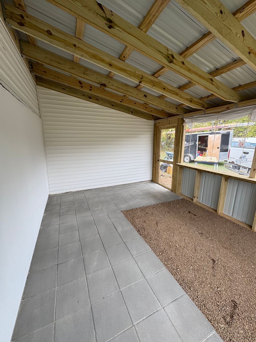 A covered outdoor patio with a gray tiled floor, a gravel section, light siding, and a wooden frame looking toward a yard.